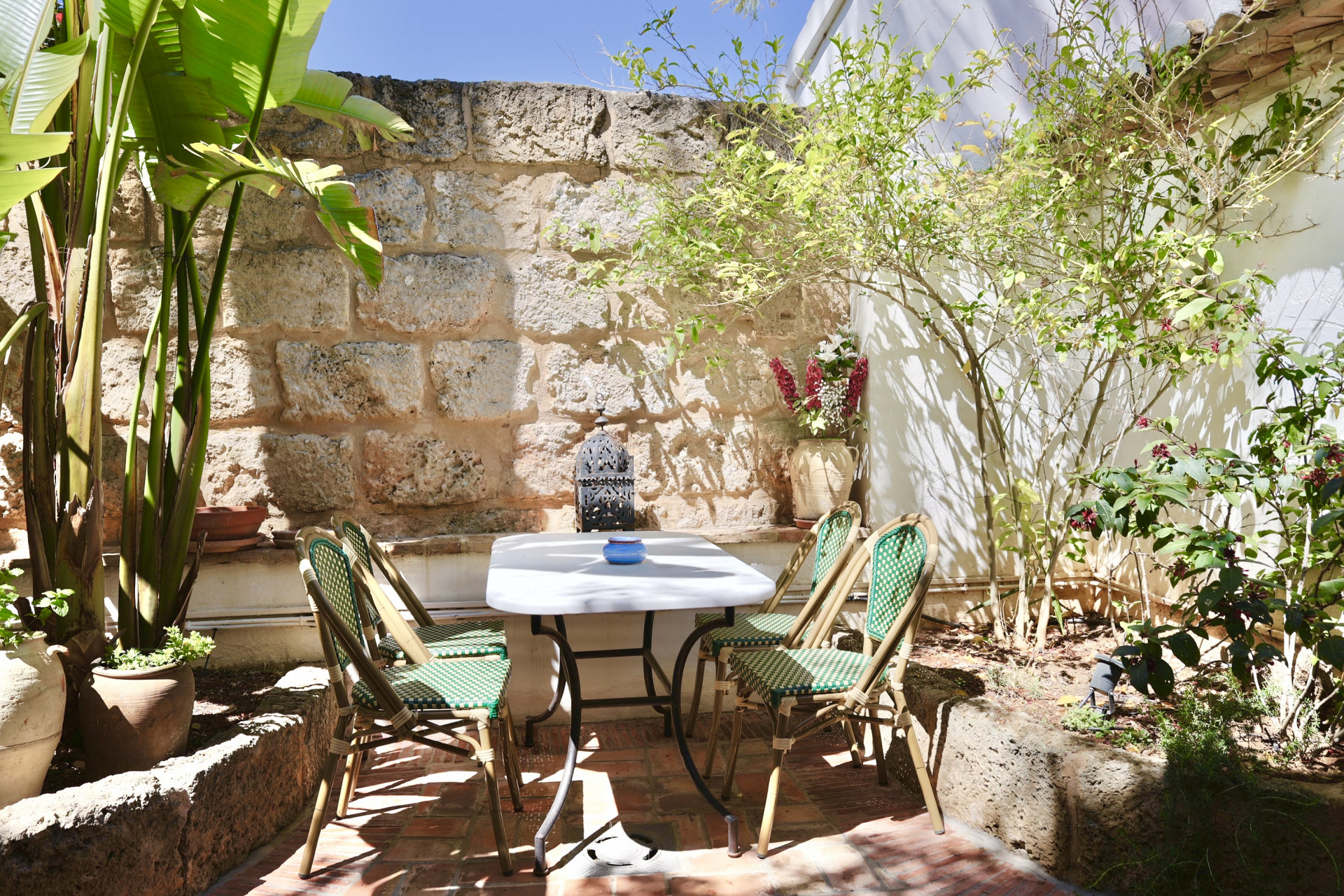 Patio avec table en marbre, chaises en osier et mur en pierre rustique. Ambiance paisible et naturelle.