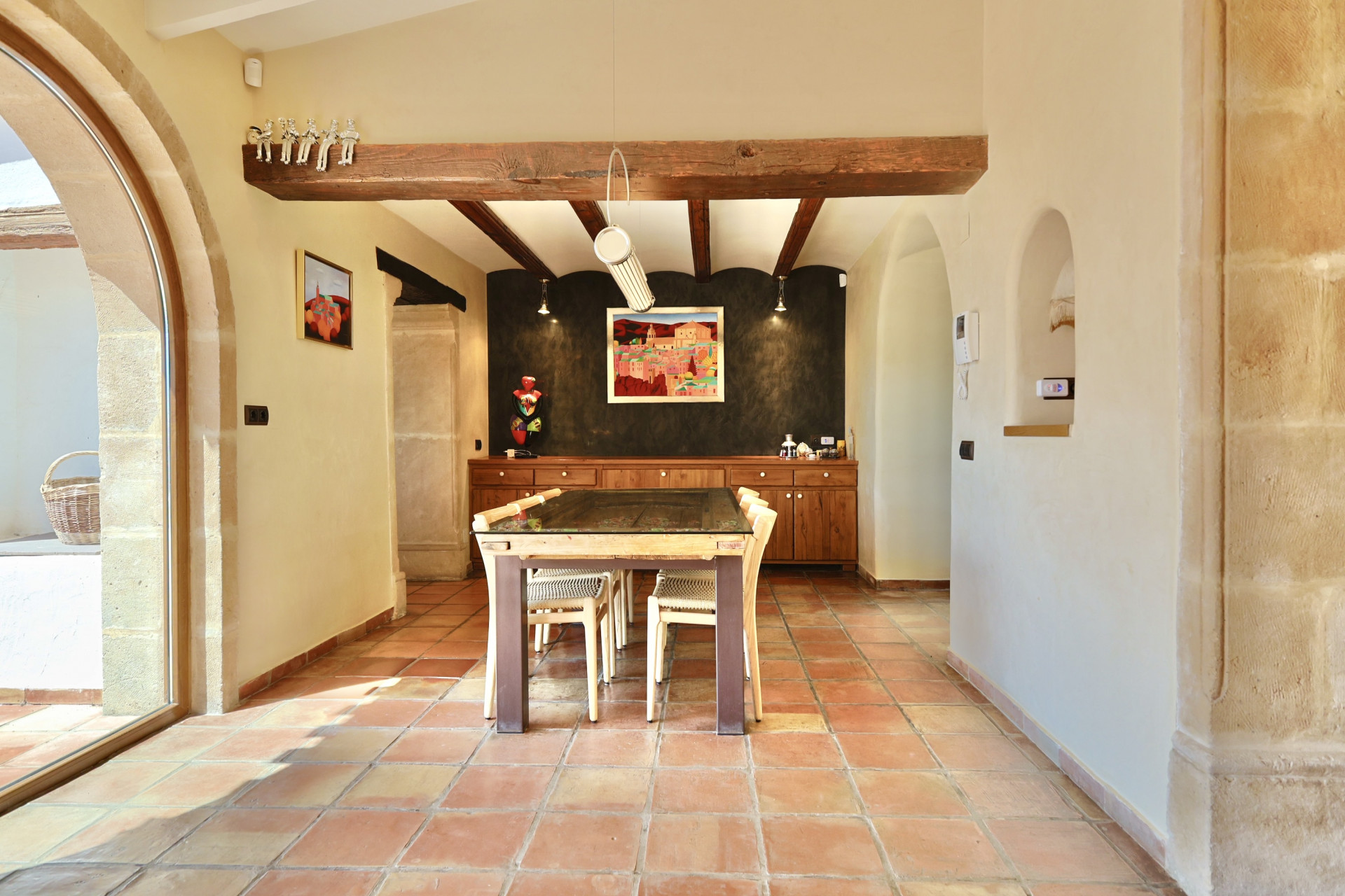 Salle à manger lumineuse avec sol en terre cuite et poutres apparentes, table à plateau en verre.