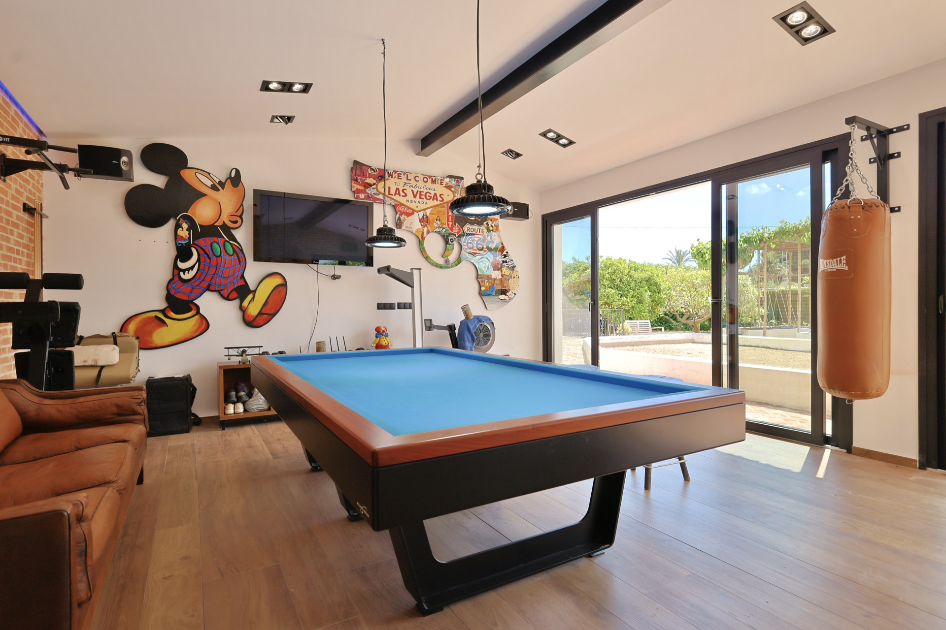 Salle de jeux avec billard bleu et décoration à thème, incluant un sac de frappe et un accès au jardin.