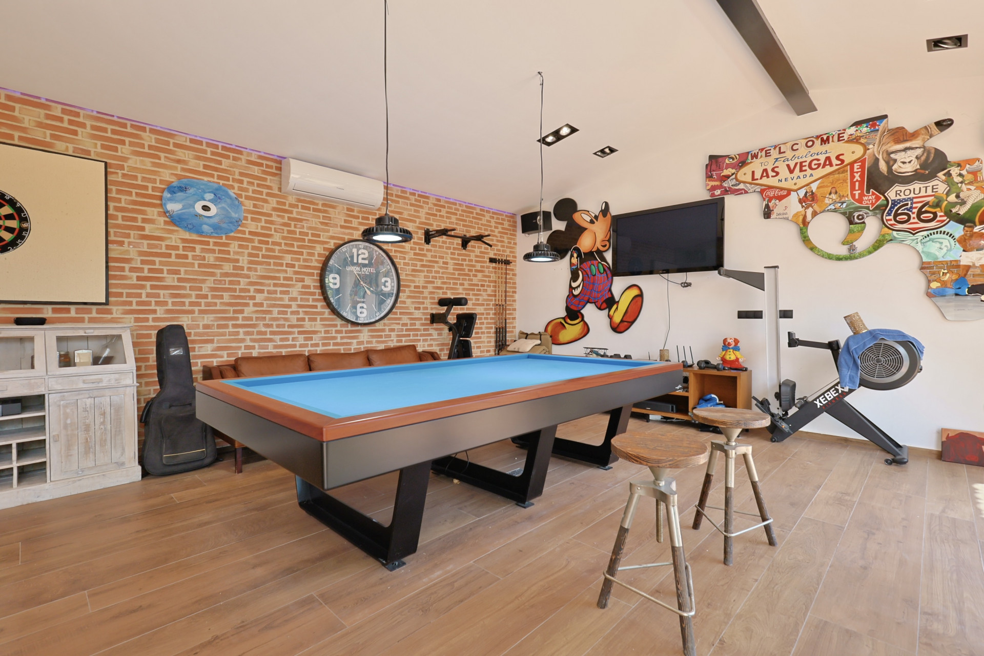 Salle de jeux avec table de billard bleue, mur en briques apparentes et décorations à thème.