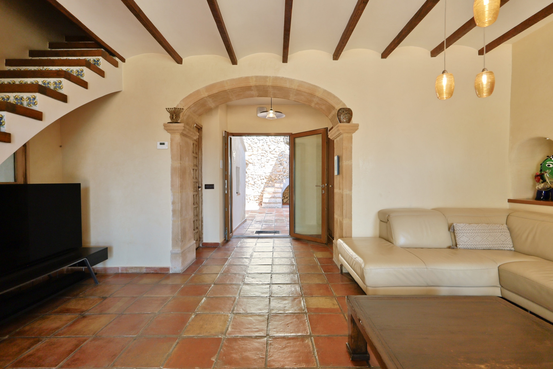 Salon avec sol en terre cuite, canapé en cuir et arche en pierre donnant sur l'extérieur.