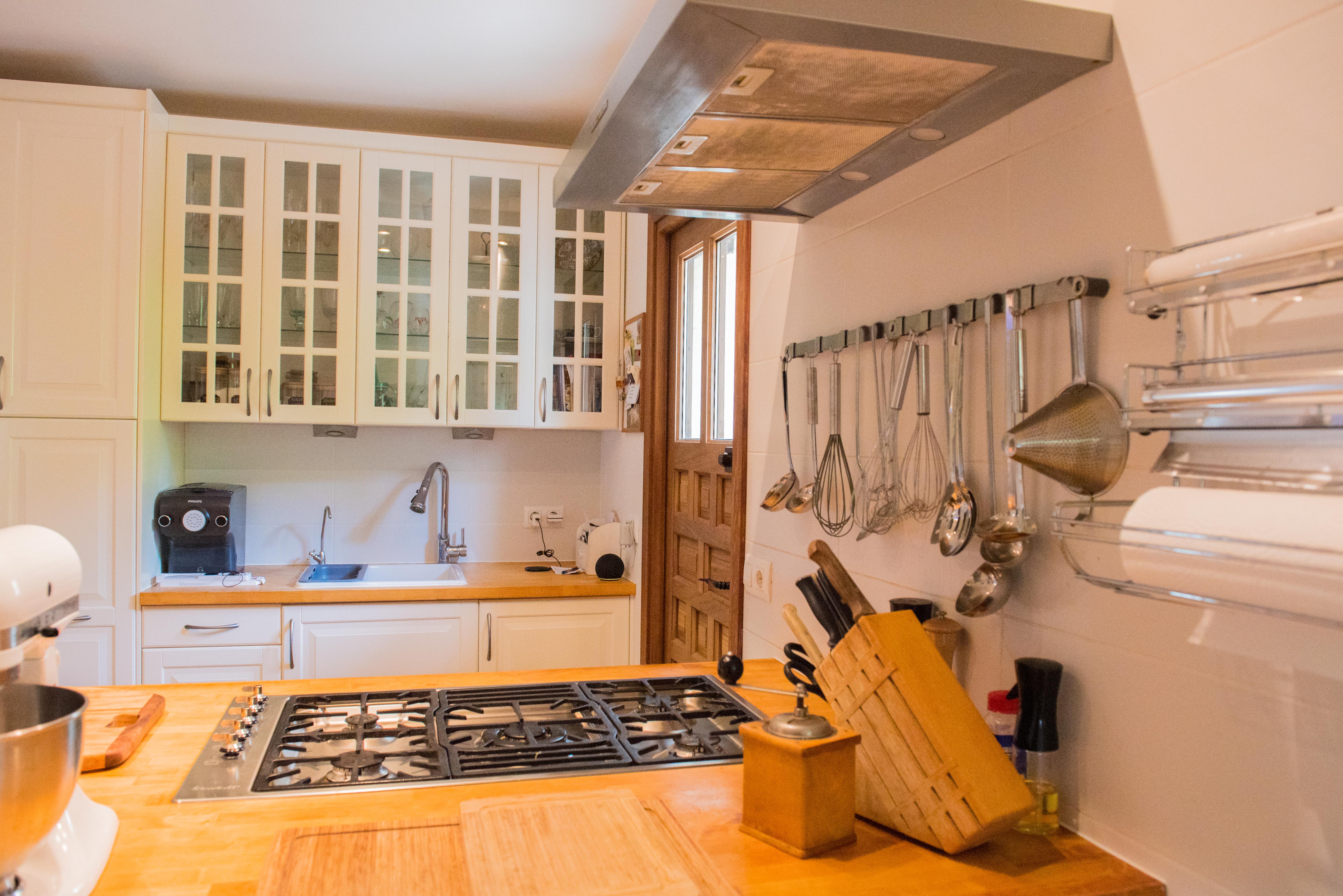 Cuisine fonctionnelle avec plans de travail en bois, plaque de cuisson au gaz intégrée et placards blancs vitrés. Comprend une zone de préparation et une porte en bois massif.