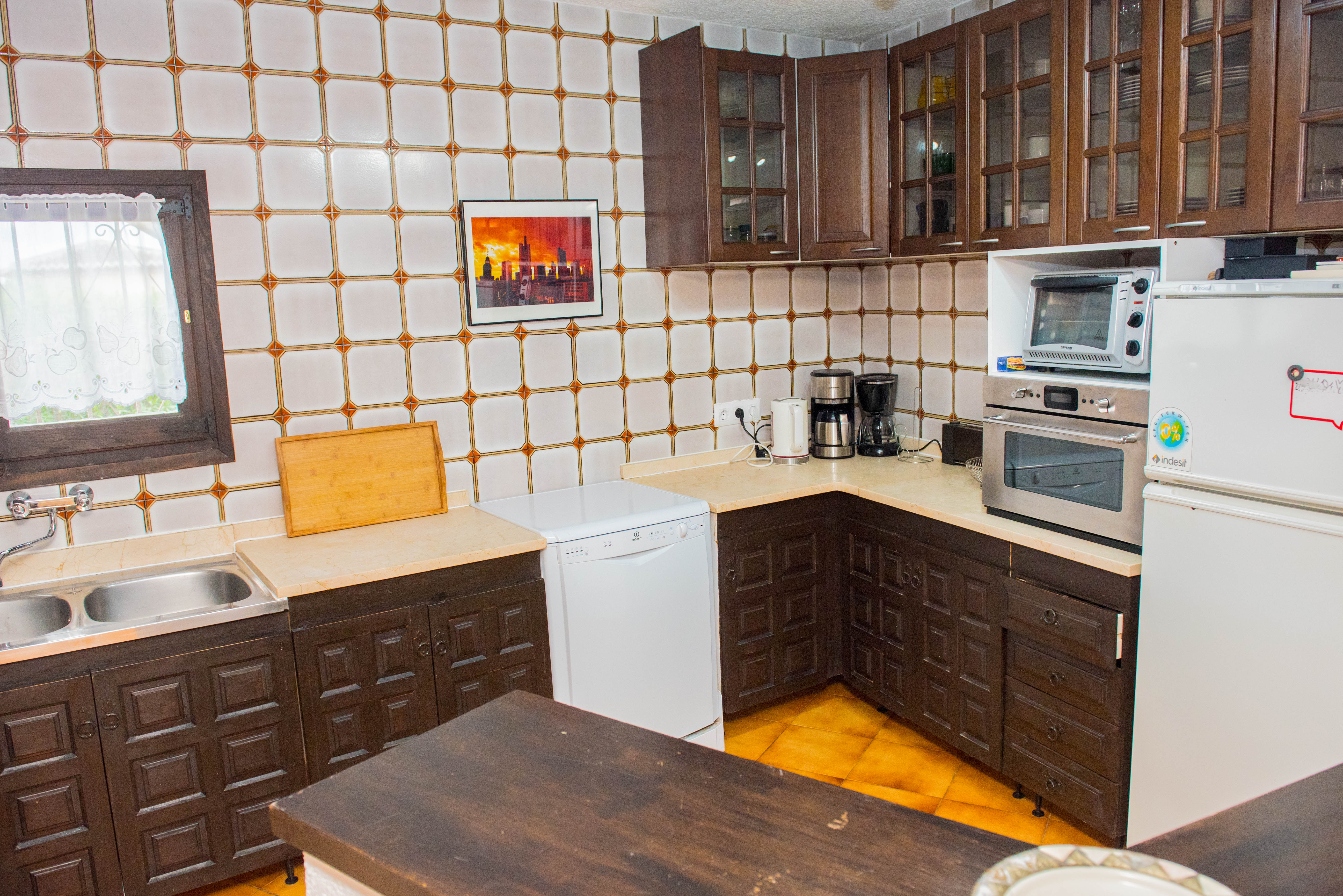 Cuisine rustique avec placards en bois foncé sculpté, plan de travail crème et carrelage mural à motifs. Équipée d'un lave-vaisselle blanc et d'un four encastré.