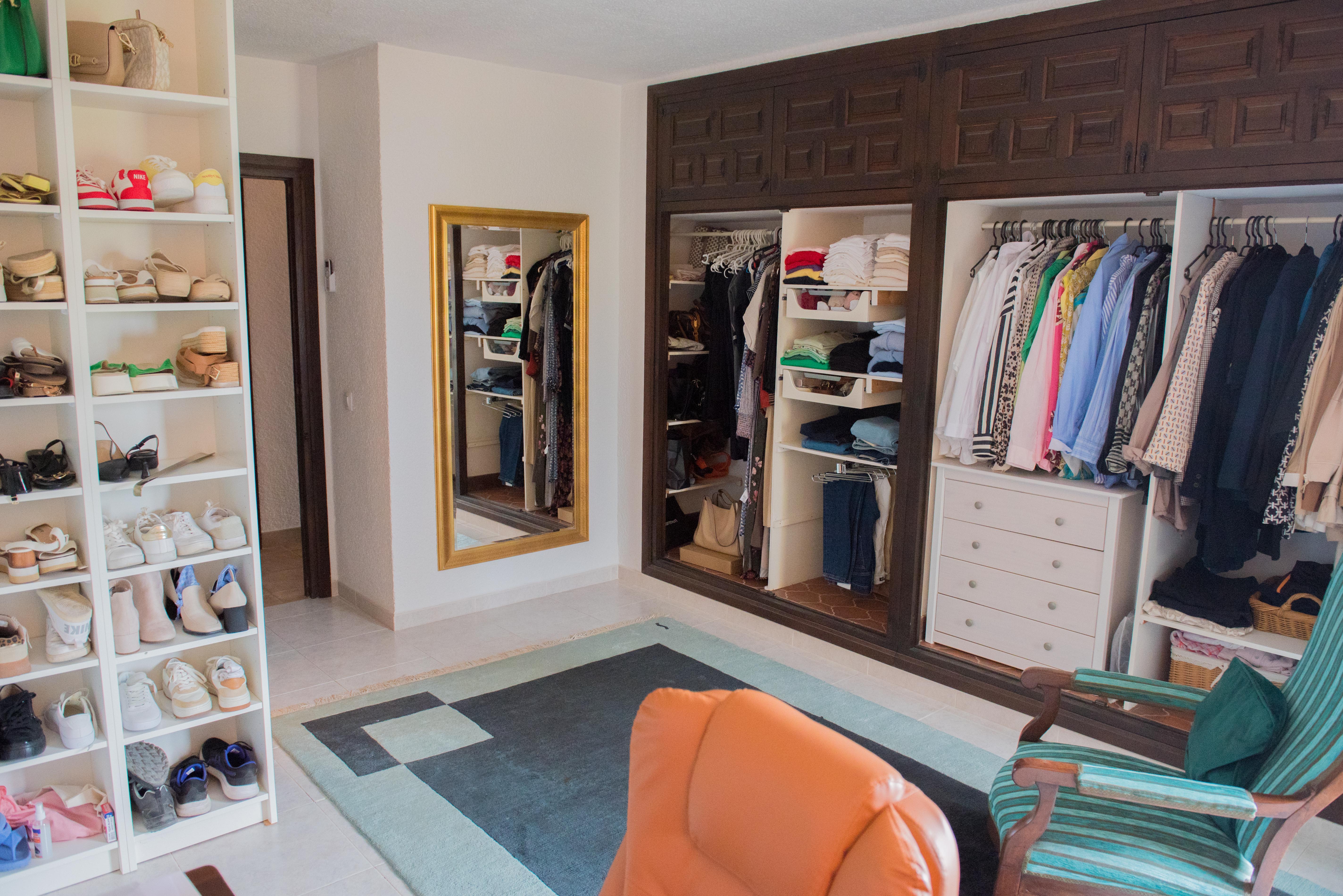 Dressing spacieux avec placards intégrés en bois sombre, étagères blanches pour chaussures, miroir en pied doré et coin salon avec tapis géométrique.