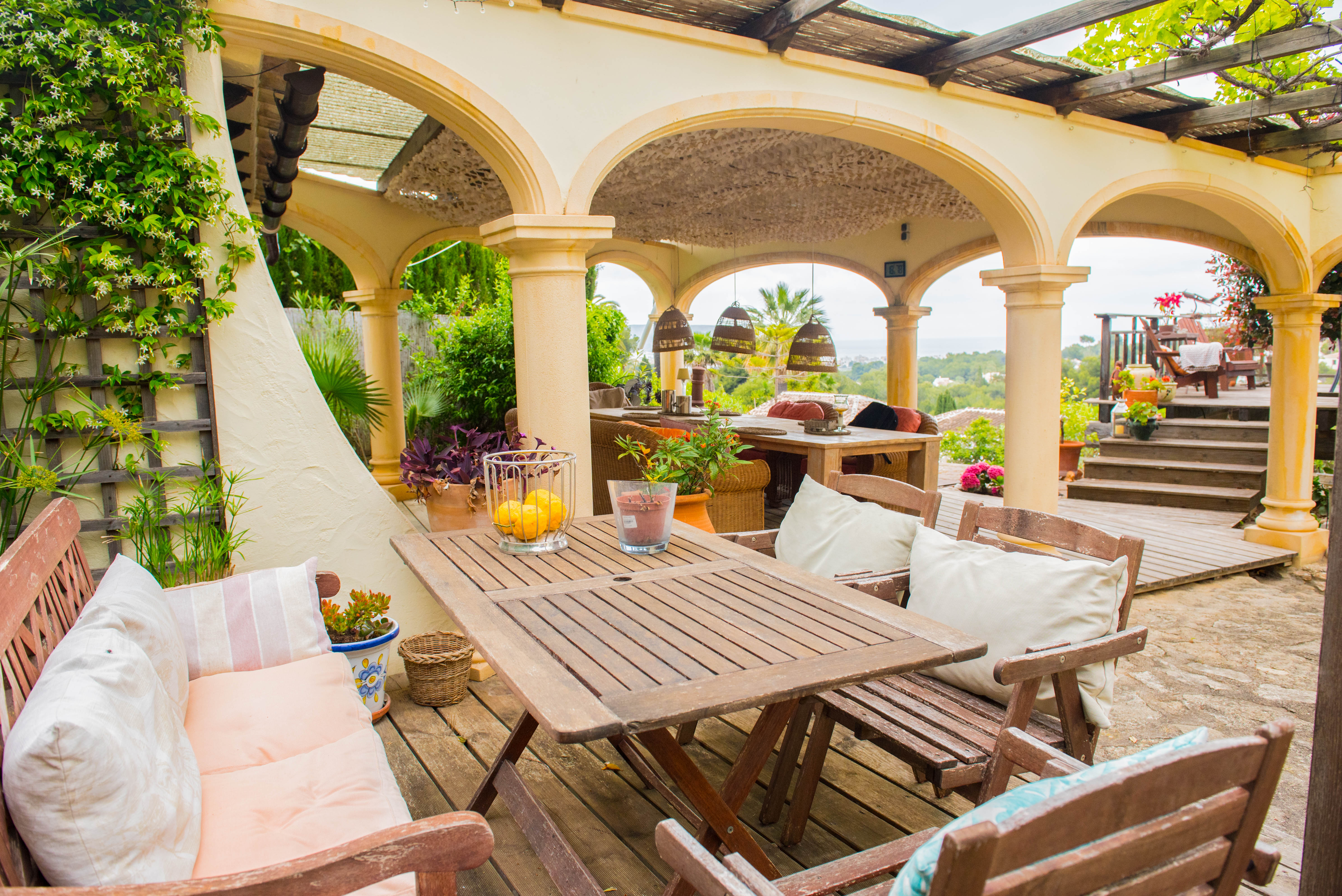 Terrasse couverte avec arches méditerranéennes, mobilier de jardin en bois, plancher en bois et vue panoramique sur la mer et la nature.