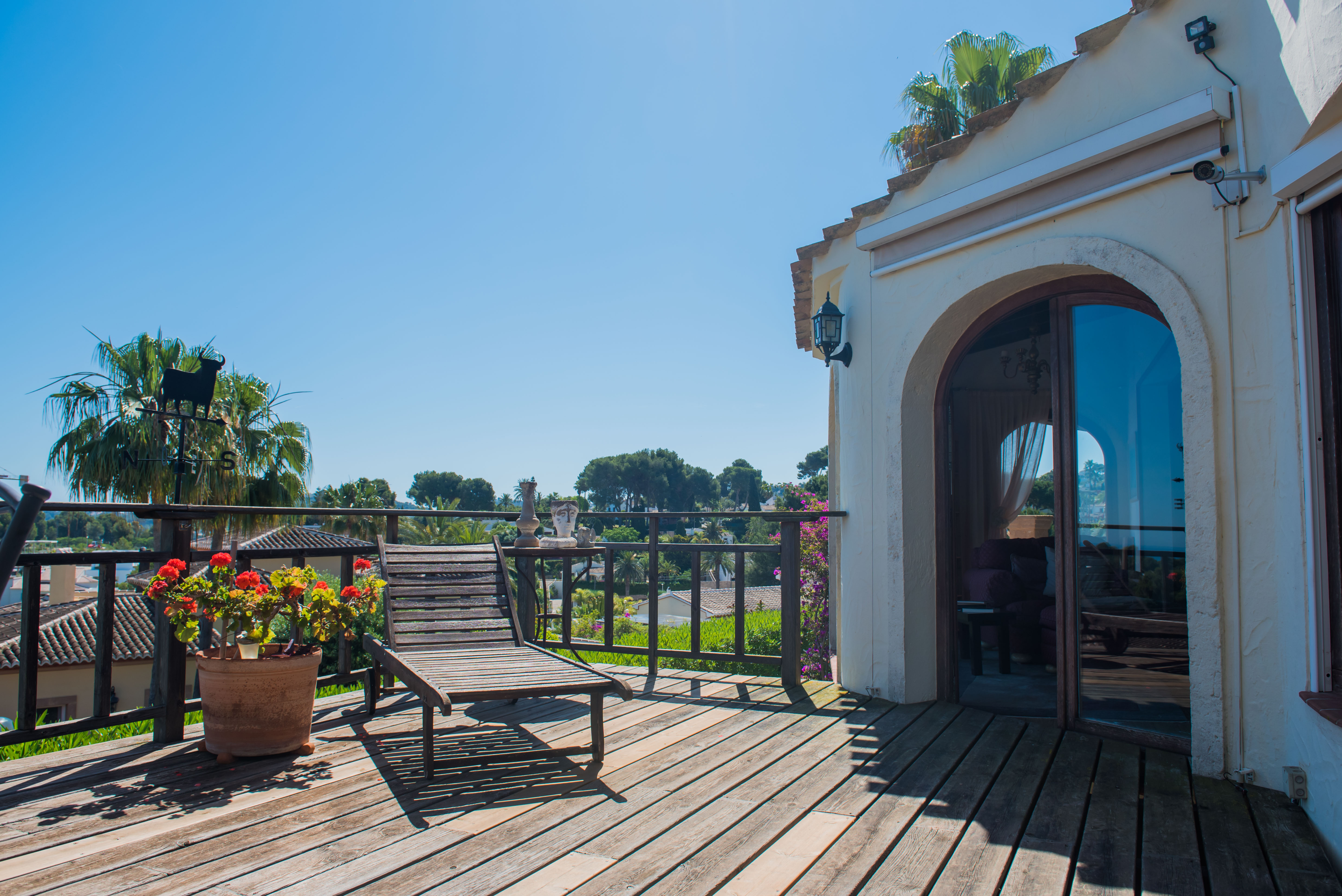Terrasse ensoleillée avec plancher en bois, chaise longue et vue sur le paysage méditerranéen.