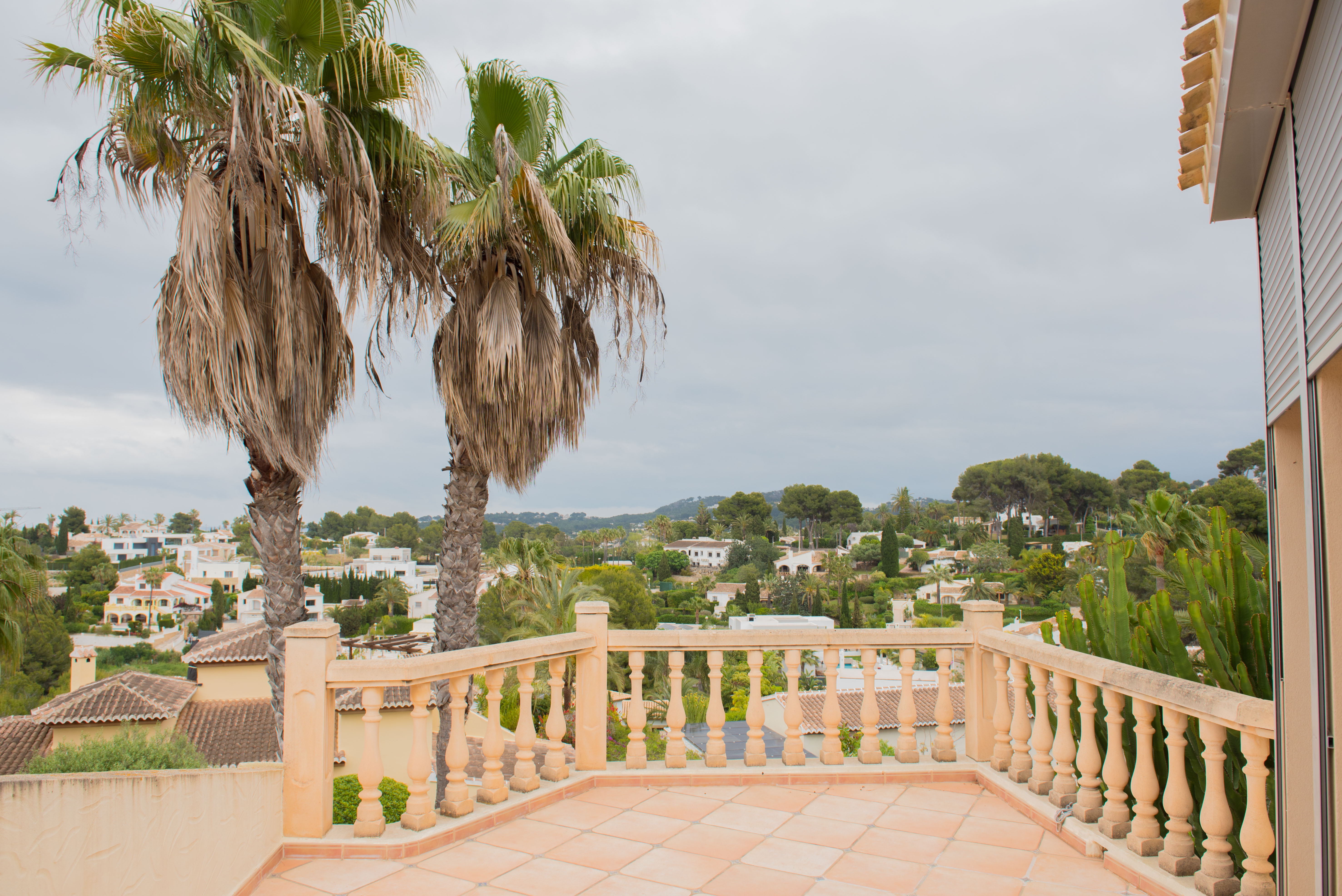 Terrasse surélevée avec balustrade classique et carrelage en terre cuite, offrant une vue panoramique sur le quartier résidentiel et les palmiers.