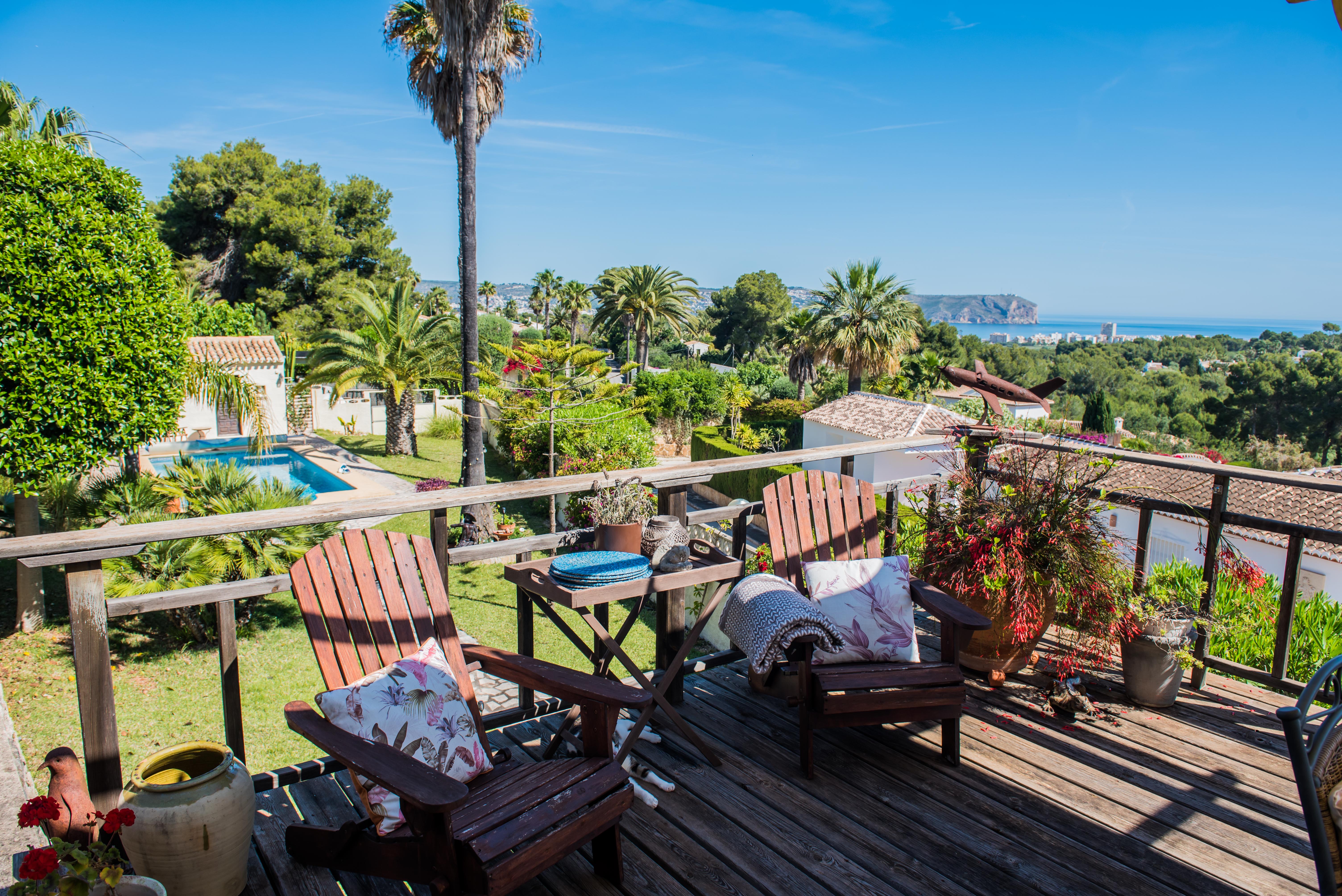 Vue depuis la terrasse en bois avec chaises Adirondack, jardins et vue panoramique sur la mer à Jávea.