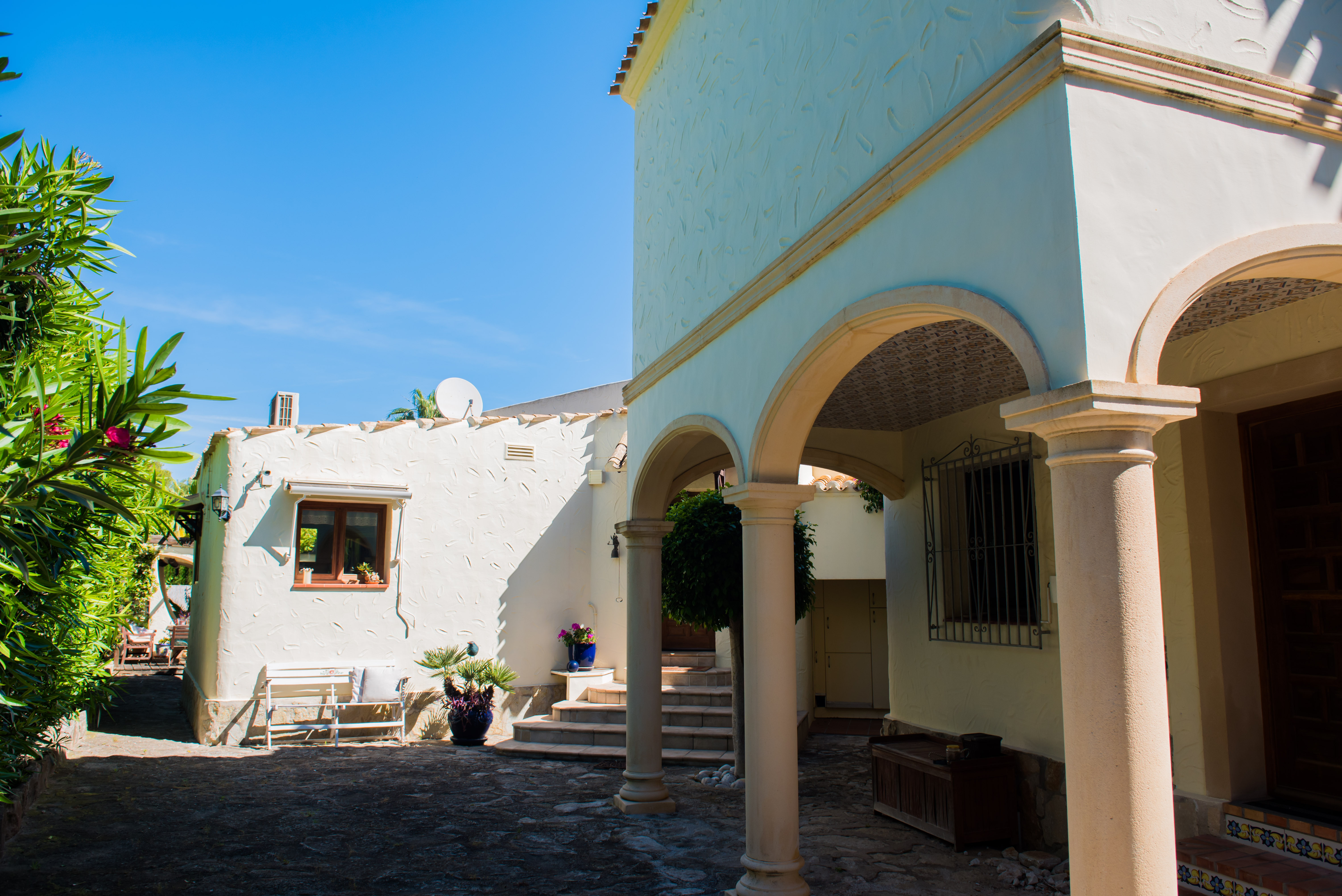 Vue extérieure de la villa avec des arcades en pierre et des murs blancs texturés, entourée de verdure méditerranéenne.