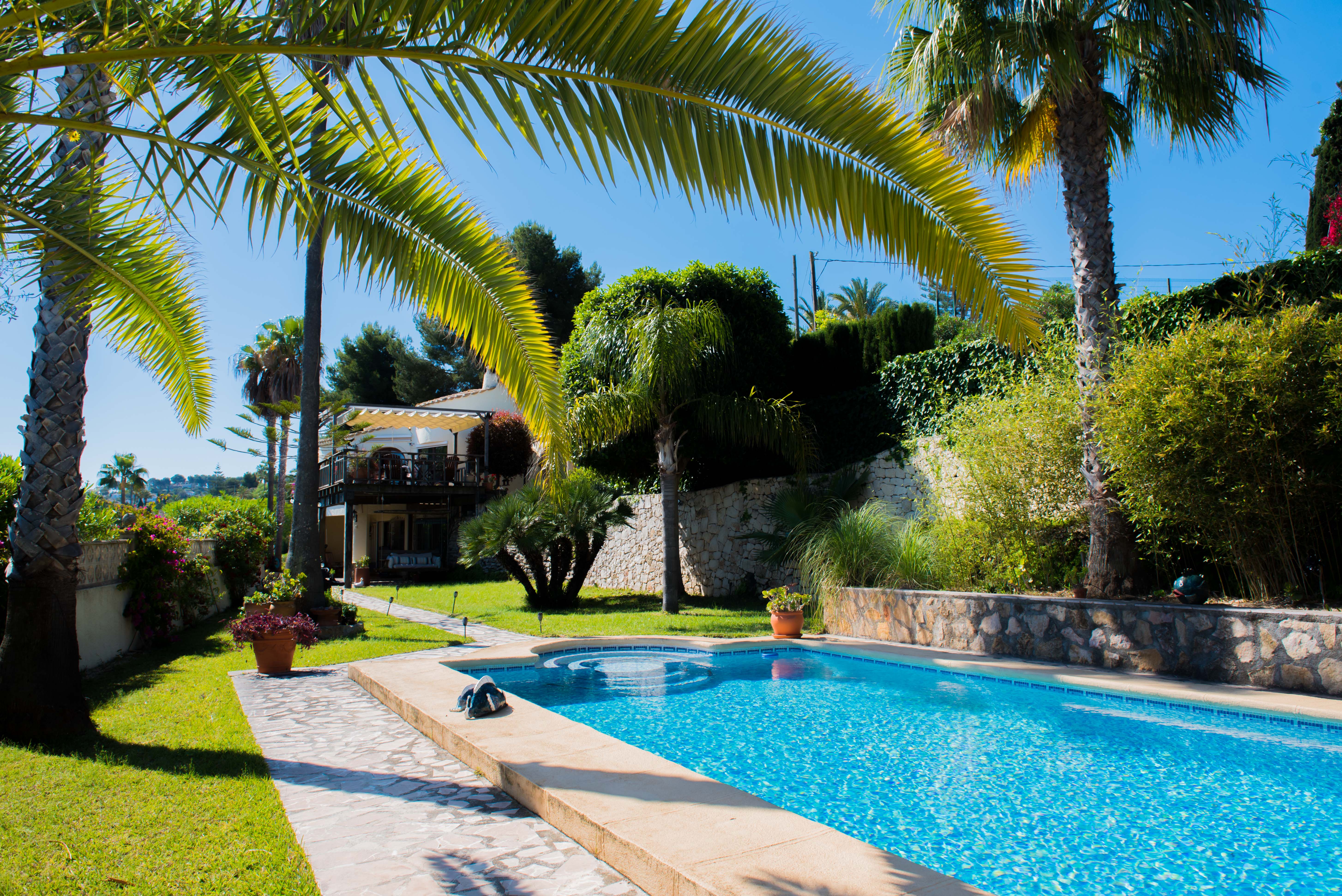 Vue sur la piscine carrelée de bleu et le jardin méditerranéen avec palmiers à Jávea.