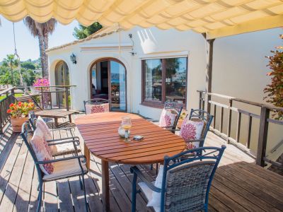 Terrasse couverte avec table en bois et chaises rembourrées, idéale pour profiter des vues panoramiques sur la mer Méditerranée.