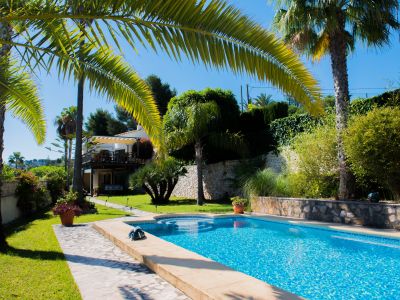 Vue sur la piscine carrelée de bleu et le jardin méditerranéen avec palmiers à Jávea.