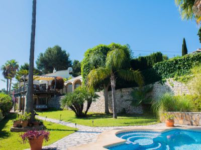Vue sur le jardin avec piscine en mosaïque bleue et chemin de pierre menant à la villa de style méditerranéen.