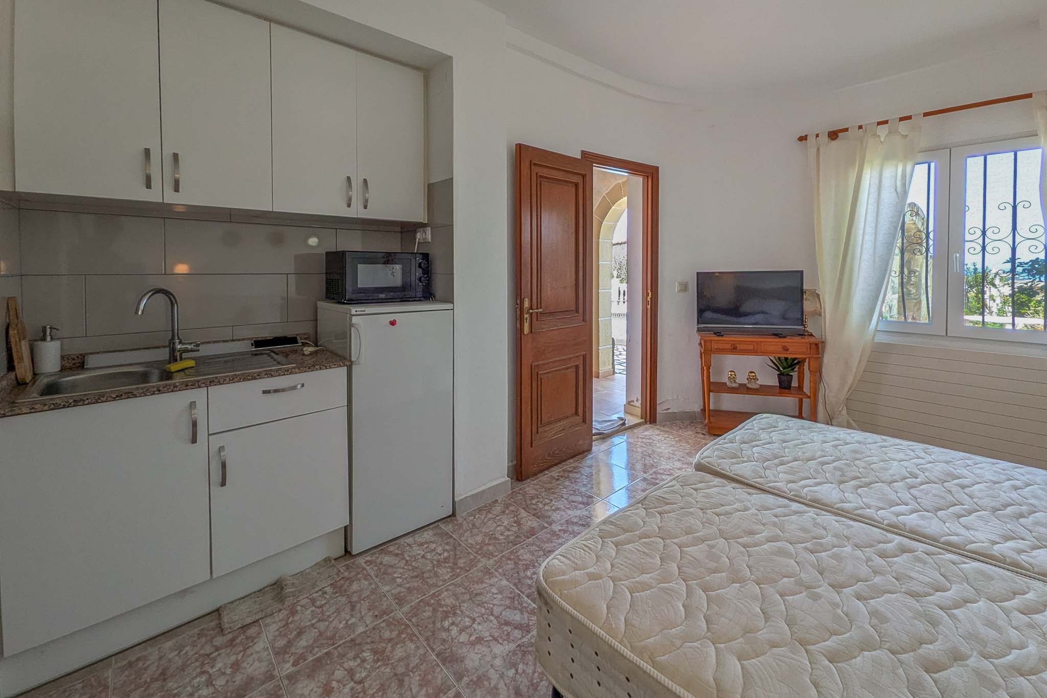 Appartement indépendant au rez-de-chaussée avec kitchenette équipée, deux lits simples et accès direct vers l'extérieur par une porte en bois massif.