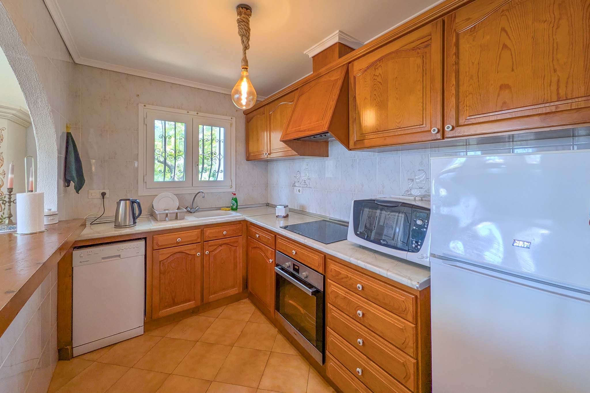 Cuisine de style rustique avec placards en bois, plan de travail en marbre et appareils intégrés. Elle dispose d'une suspension en corde et d'une fenêtre lumineuse.