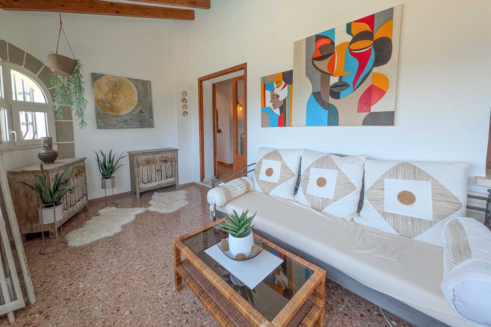 Espace de vie lumineux avec poutres en bois apparentes, sol en terrazzo et fenêtre en arc. La pièce allie mobilier rustique, art moderne et une belle luminosité naturelle.