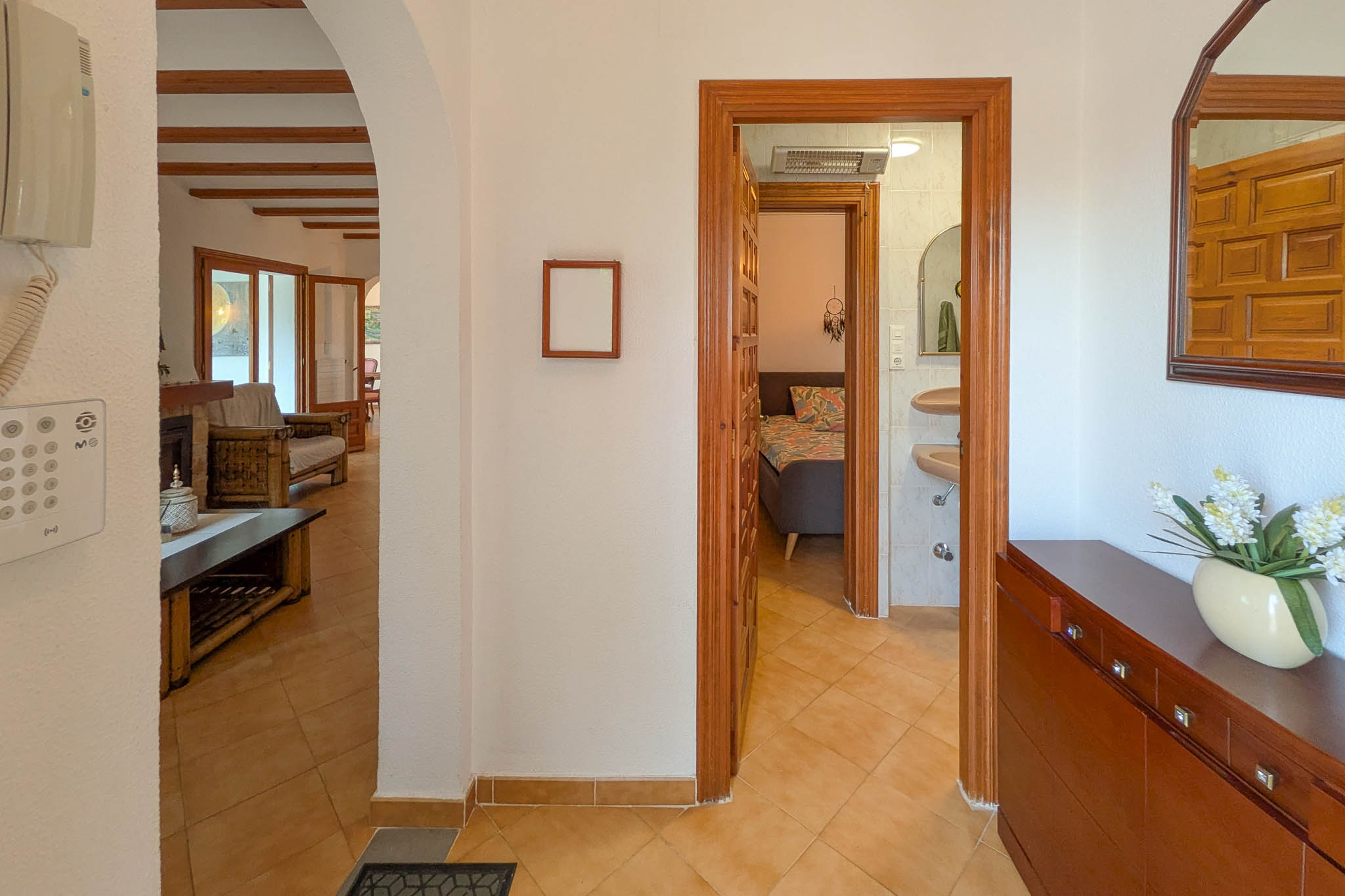 Hall de distribution avec sol en grès, reliant le salon aux poutres apparentes à une chambre et une salle de bain via des encadrements de portes en bois massif.
