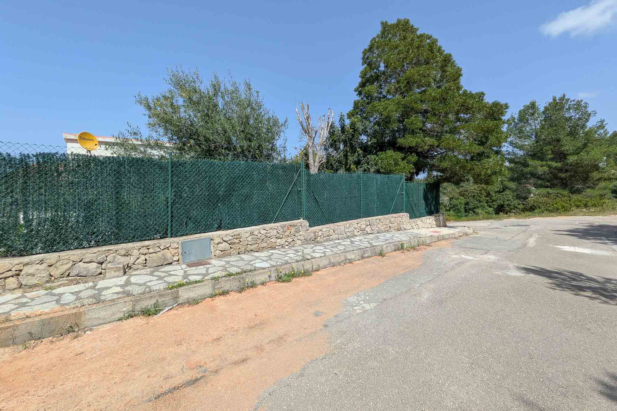 Limite extérieure avec mur en pierre naturelle, clôture d'occultation verte et trottoir pavé dans une rue résidentielle calme.