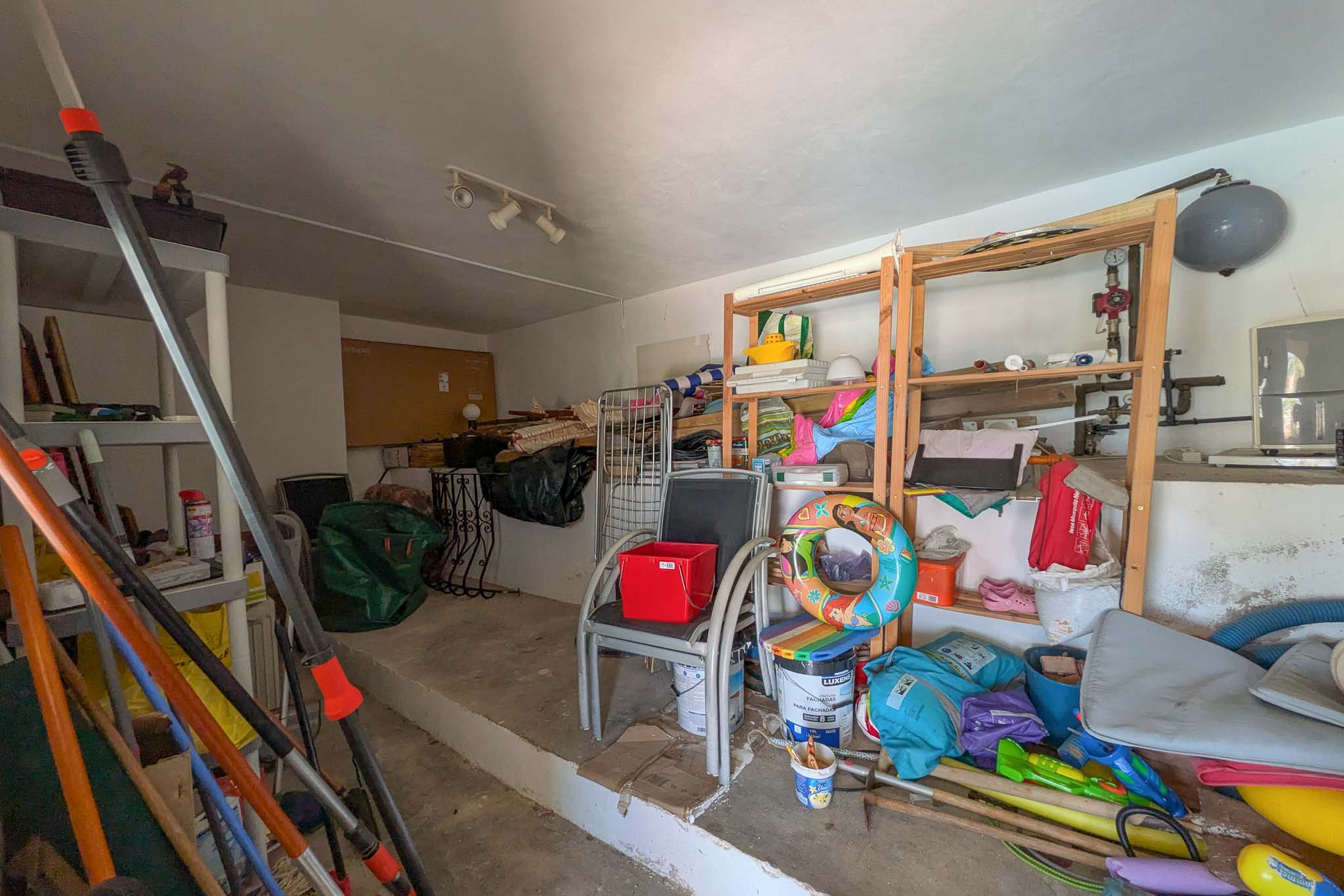 Pièce de rangement polyvalente avec sol en béton, étagères en bois et plastique, idéale pour le stockage de matériel domestique et de jardin.