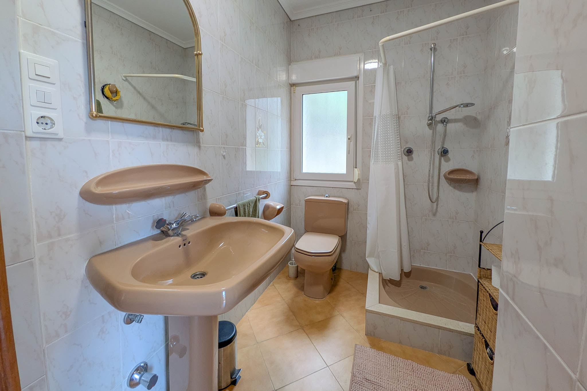 Salle de bain avec sanitaires beiges, receveur de douche avec rideau, murs entièrement carrelés et fenêtre offrant une luminosité naturelle.