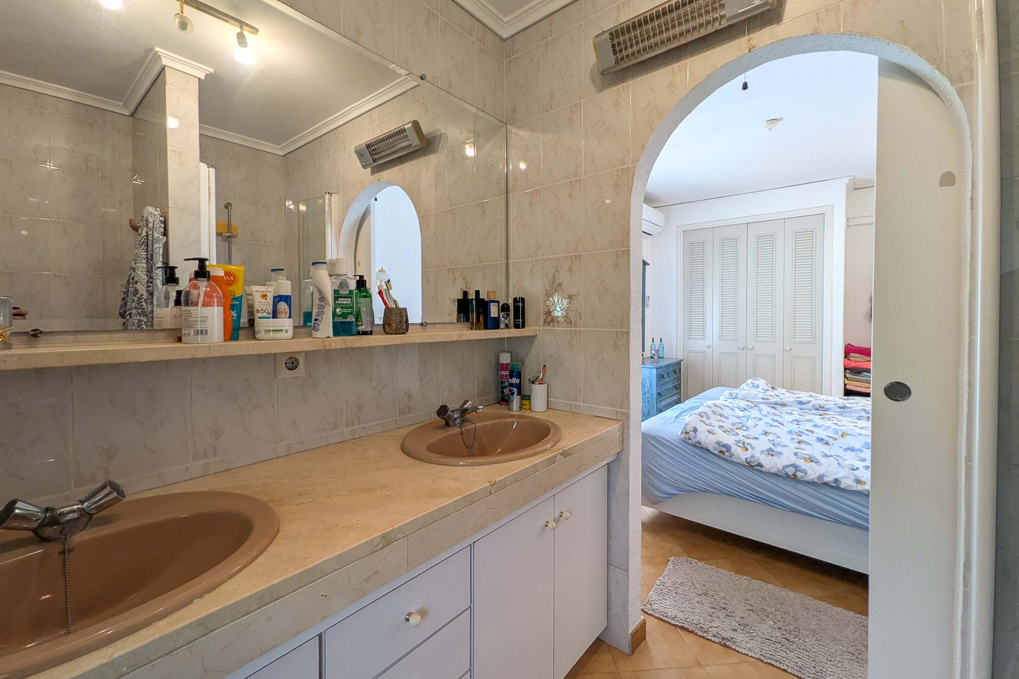 Salle de bains attenante avec double vasque sur plan de travail en marbre, reliée à la chambre par une ouverture en arche.
