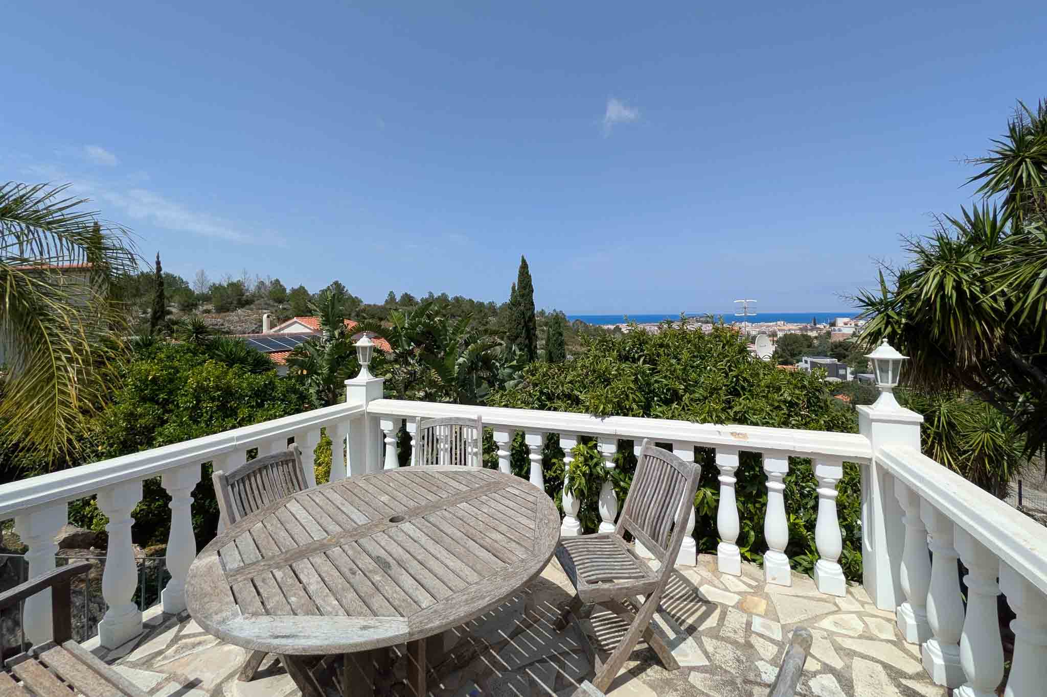Terrasse avec balustrade blanche et mobilier en bois sur sol en pierre, offrant une vue dégagée sur la mer Méditerranée et le paysage urbain de Dénia.