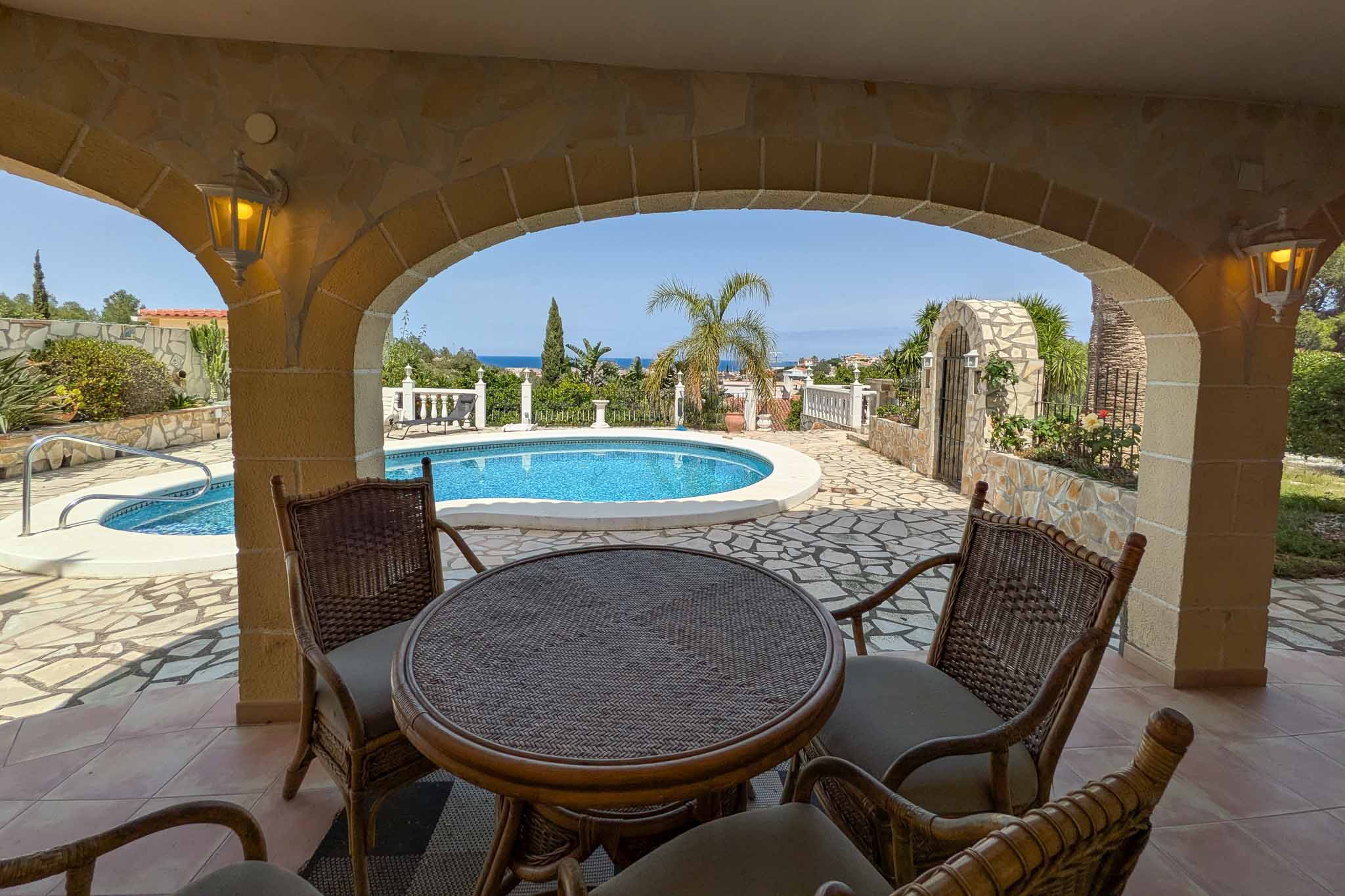 Terrasse couverte avec arches en pierre et mobilier en rotin, offrant une vue sur la piscine et l'horizon de la mer Méditerranée.