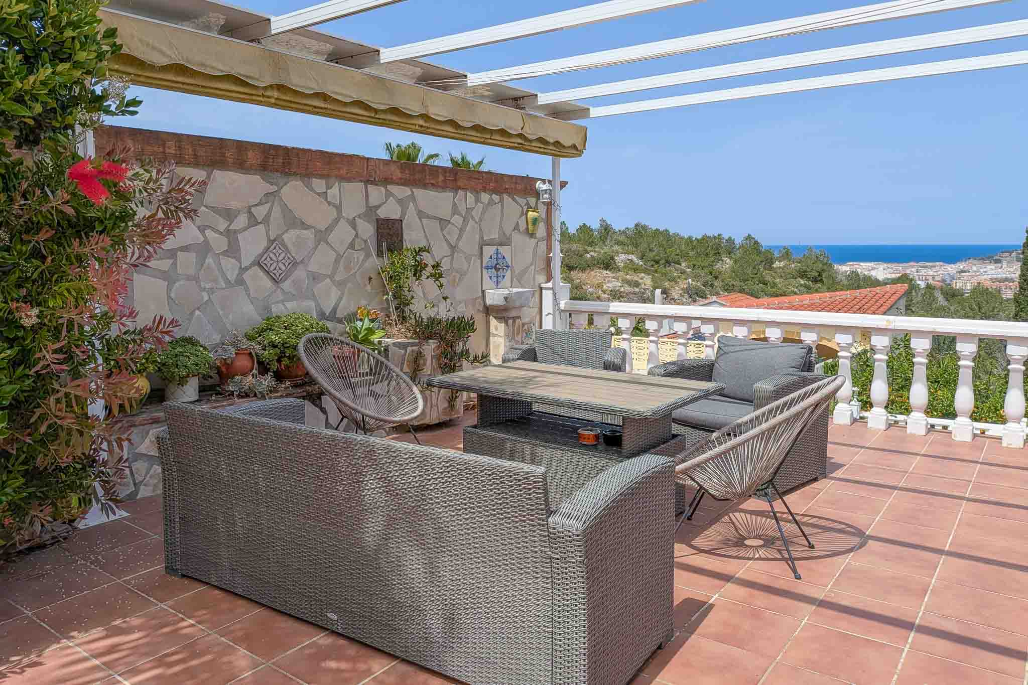 Terrasse extérieure avec salon en rotin, sol en terre cuite et vue panoramique sur la mer. Équipée d'une pergola à store et d'un mur en pierre naturelle décorative.