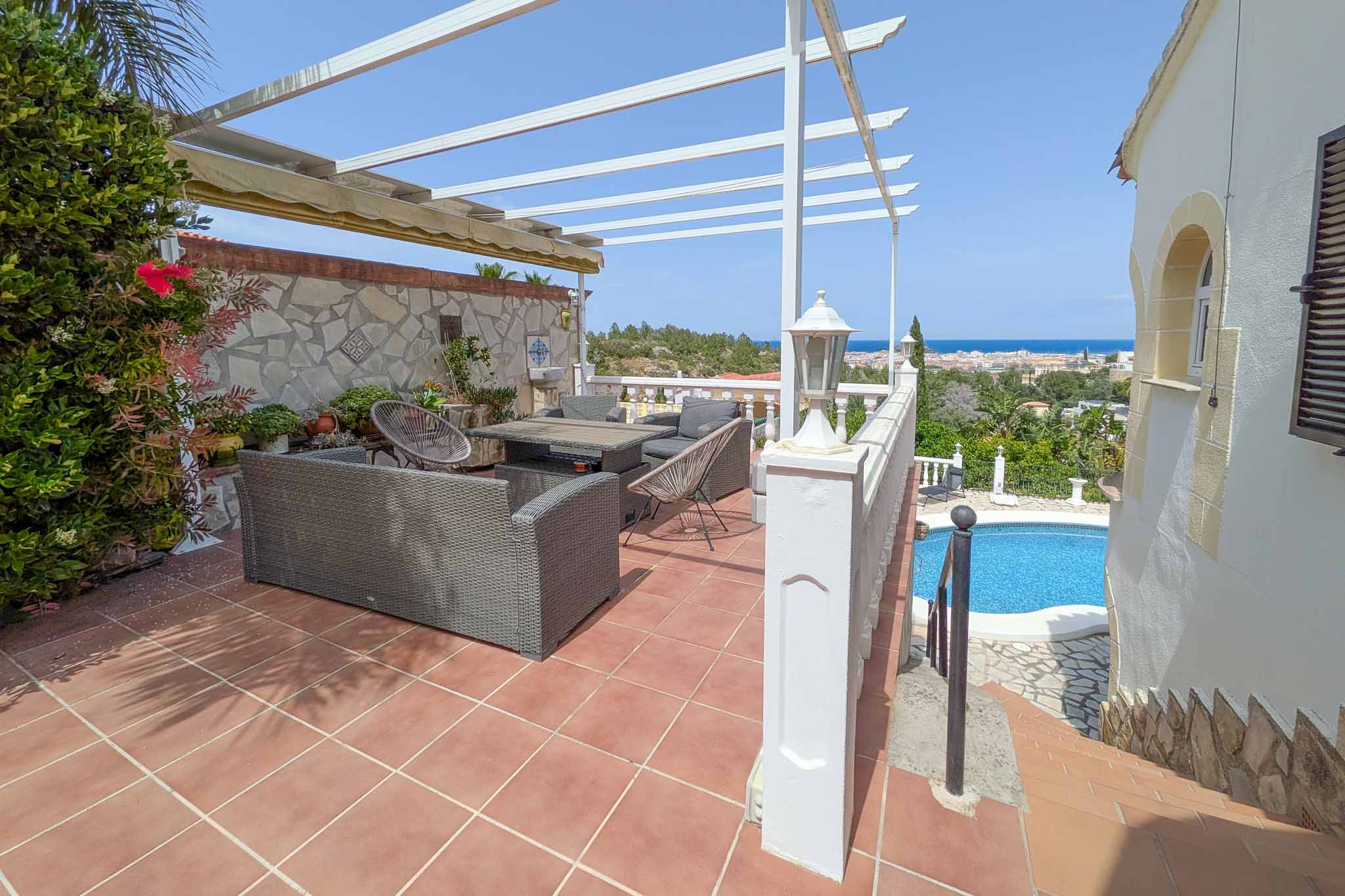 Terrasse supérieure avec salon de jardin, pergola blanche et vues panoramiques sur la Méditerranée et Dénia, surplombant l'espace piscine.
