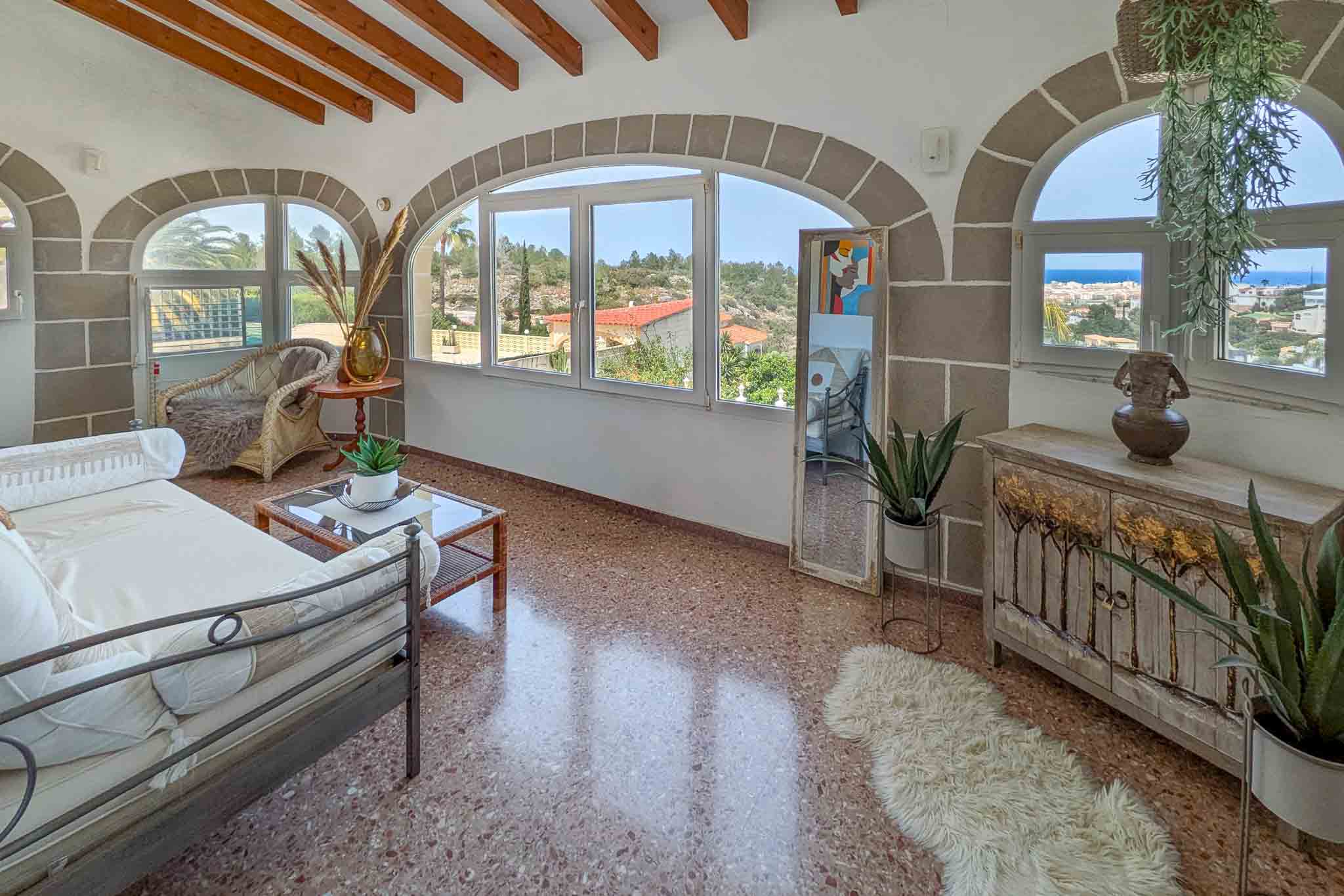 Terrasse vitrée avec arches en pierre, poutres en bois apparentes et sol en terrazzo. Elle offre une vue panoramique sur la mer Méditerranée et Dénia.