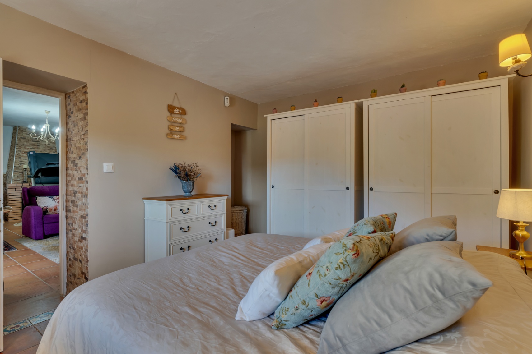 Chambre chaleureuse avec de grands placards blancs, une commode classique et un mur en pierre naturelle ouvrant sur l'espace de vie.