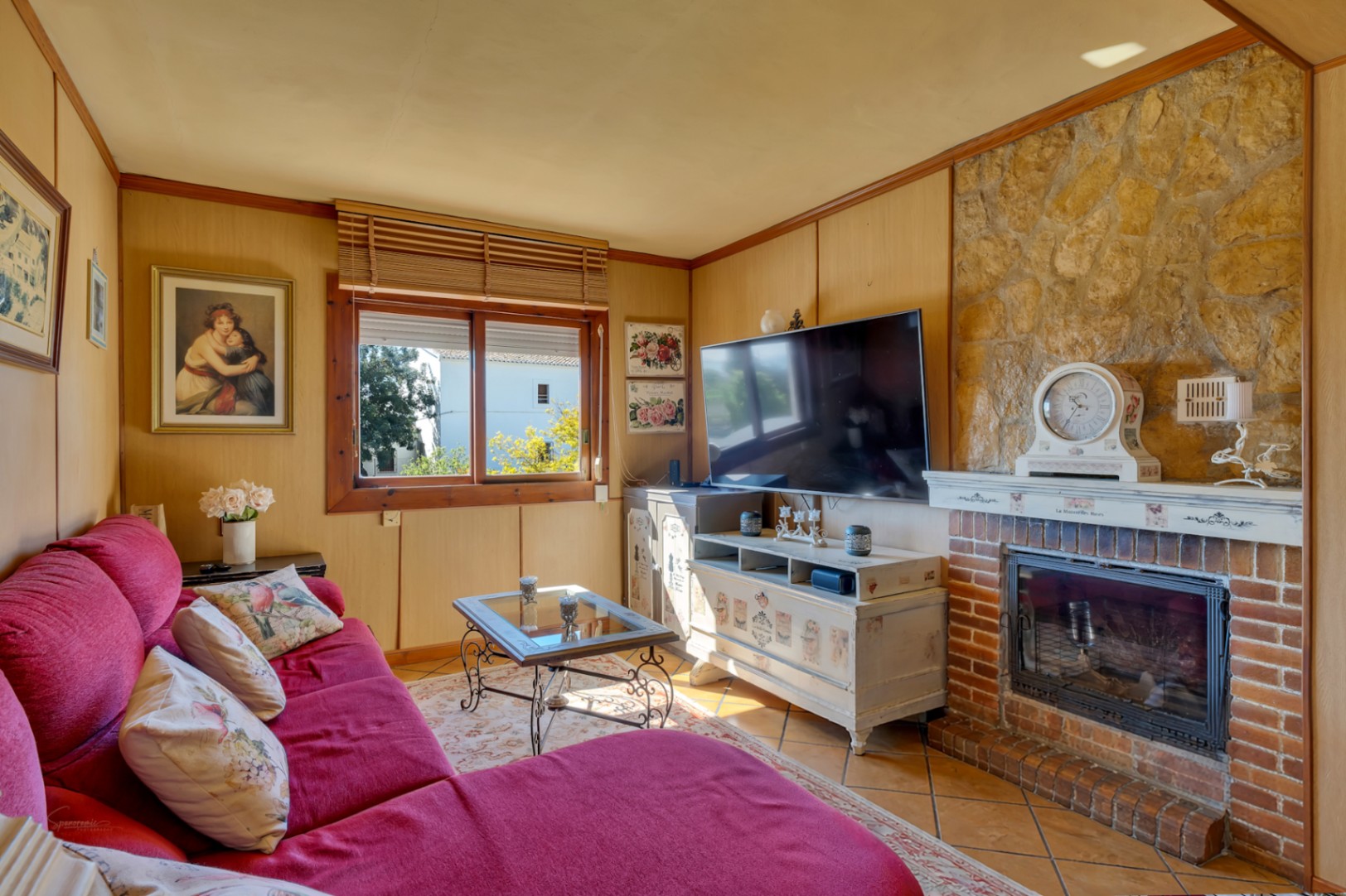 Espace de vie chaleureux avec cheminée en brique et pierre, murs habillés de bois et canapé rouge offrant une atmosphère rustique.
