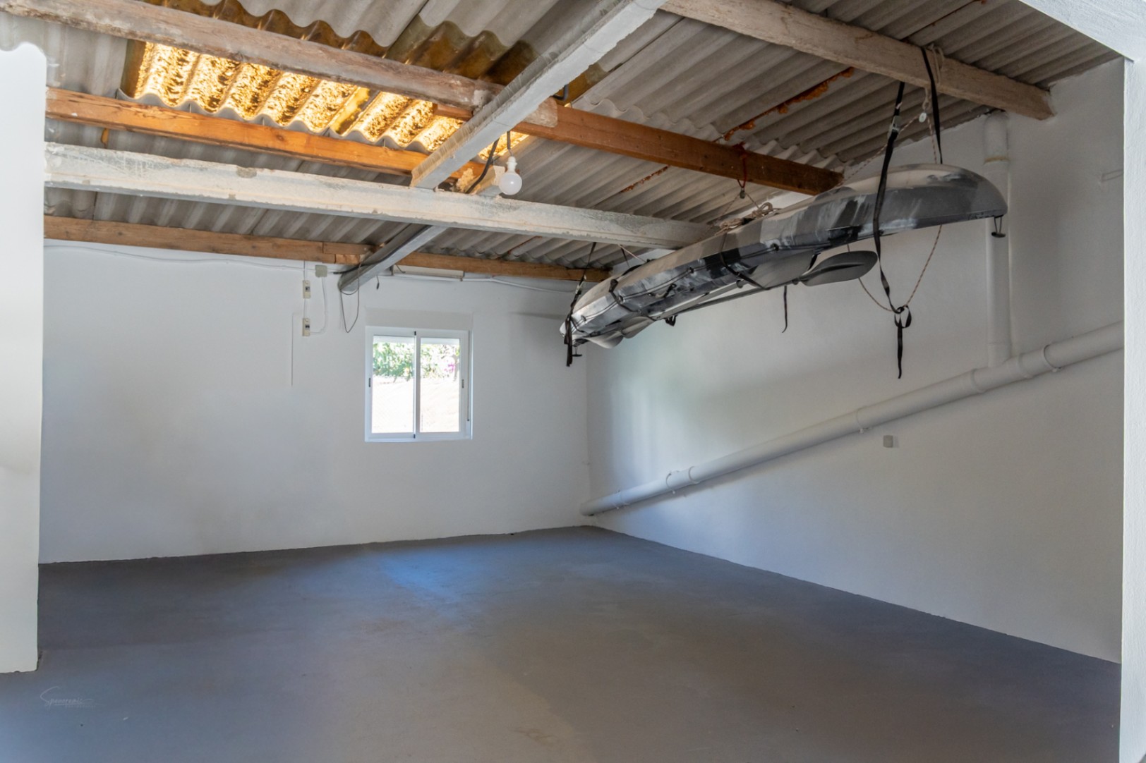 Garage fermé avec sol gris et poutres en bois, équipé d'un système de rangement pour kayak et d'un toit ondulé laissant passer la lumière.