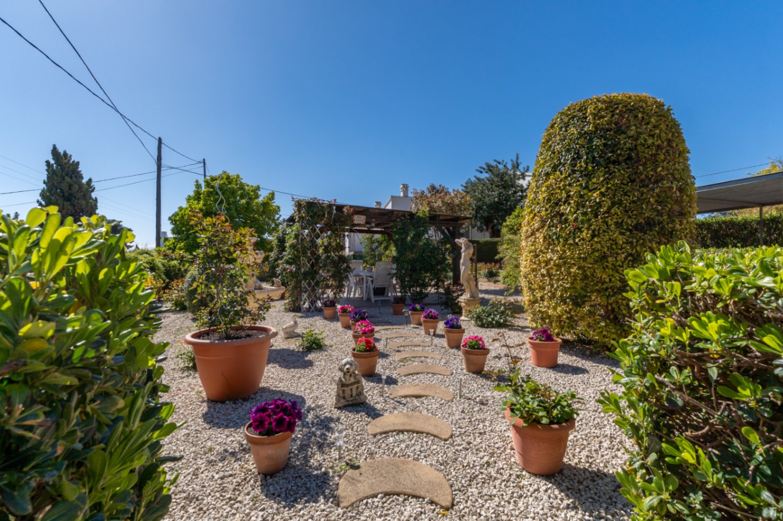 Jardin méditerranéen avec gravier, pas japonais incurvés et pots en terre cuite. Une pergola en bois abrite un espace de détente extérieur.