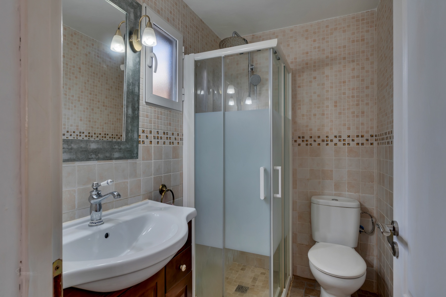 Salle de bains comprenant un lavabo sur meuble en bois, un miroir au cadre rustique et une cabine de douche d'angle avec parois en verre dépoli.