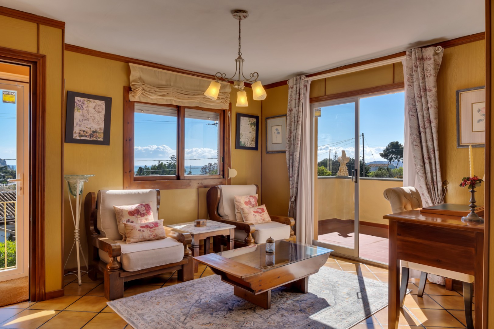 Salon lumineux avec fauteuils en bois, table basse vitrée et accès direct à une terrasse offrant une vue dégagée sur la mer Méditerranée.