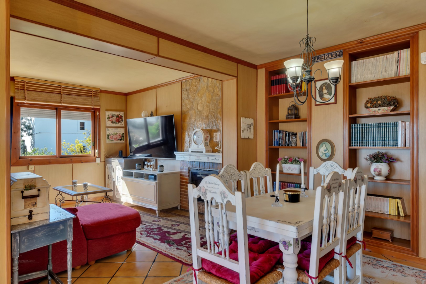 Salon-salle à manger avec cheminée en pierre, murs lambrissés et bibliothèques intégrées. Comprend un mobilier de style rustique et un sol en grès cérame.