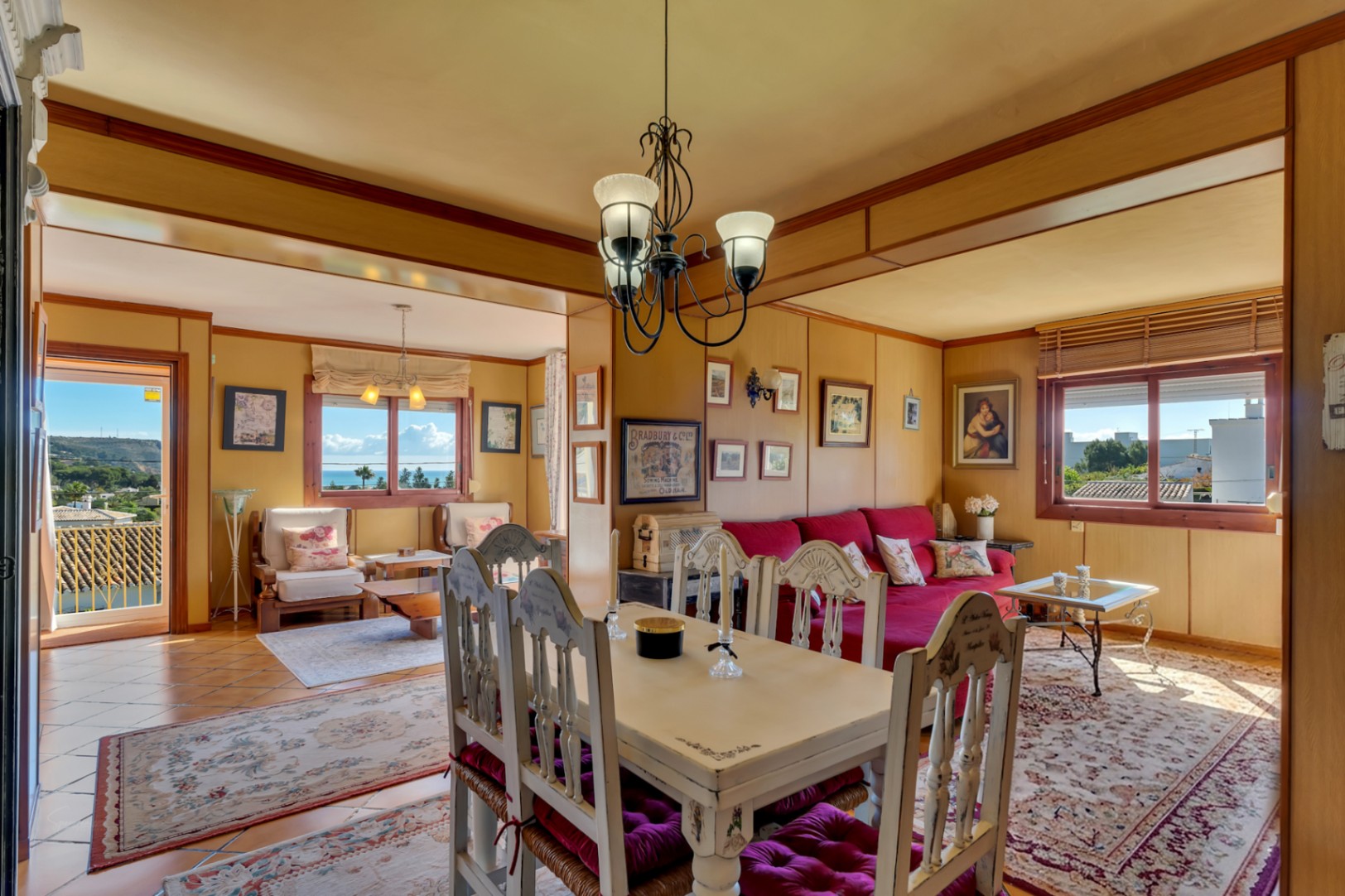 Salon-salle à manger rustique avec murs lambrissés, mobilier classique et accès direct à une terrasse offrant une vue imprenable sur la mer Méditerranée.
