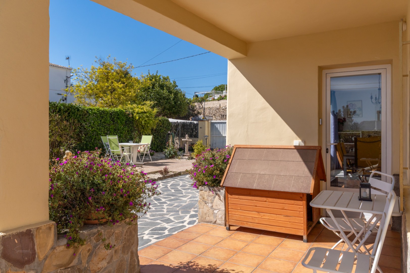 Terrasse couverte avec sol en terre cuite, mobilier d'extérieur et vue sur le jardin paysager avec son chemin en dalles de pierre.