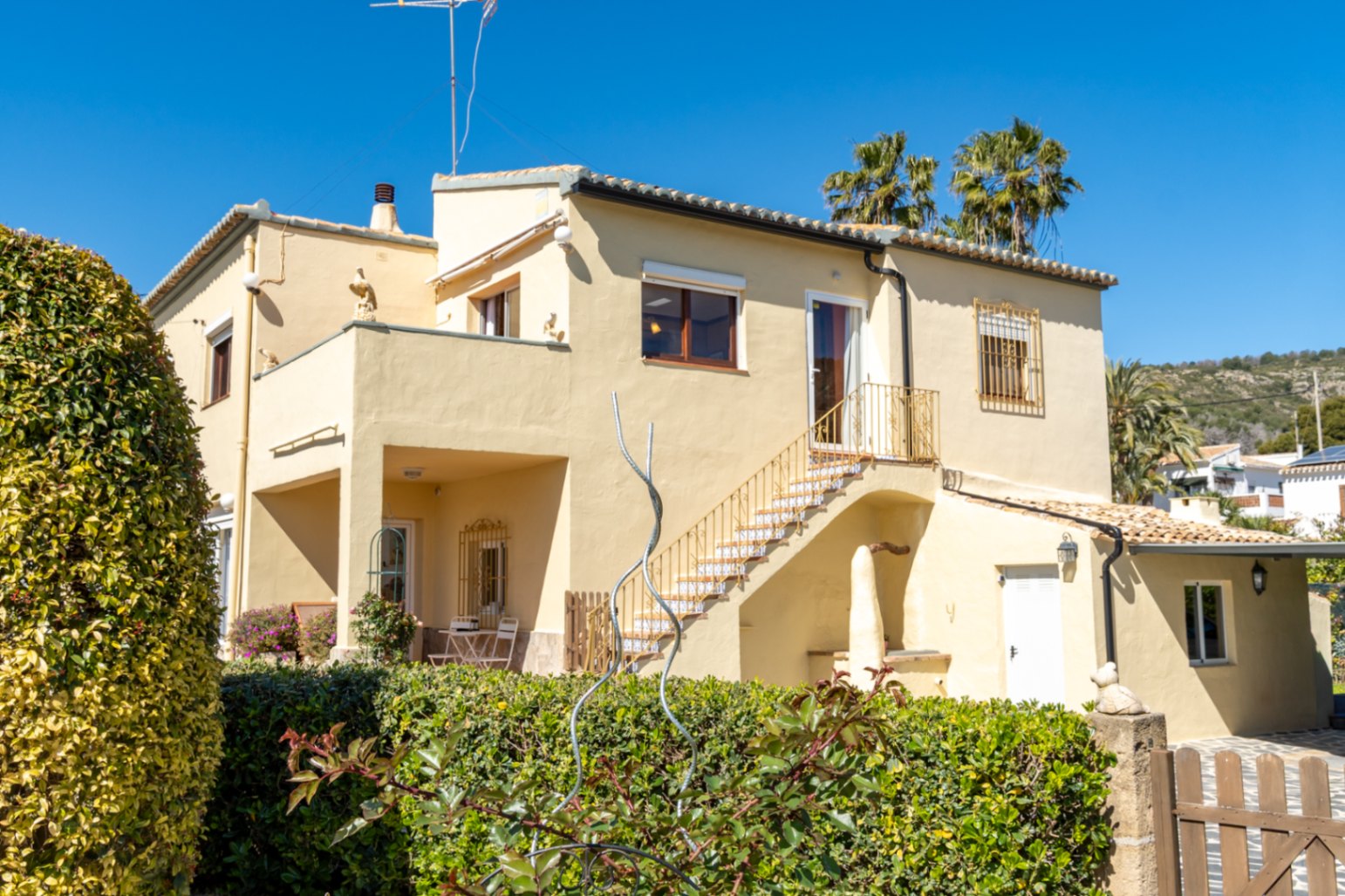 Vue extérieure de la villa avec sa façade crème, son escalier extérieur orné de carreaux traditionnels et ses terrasses réparties sur deux niveaux.
