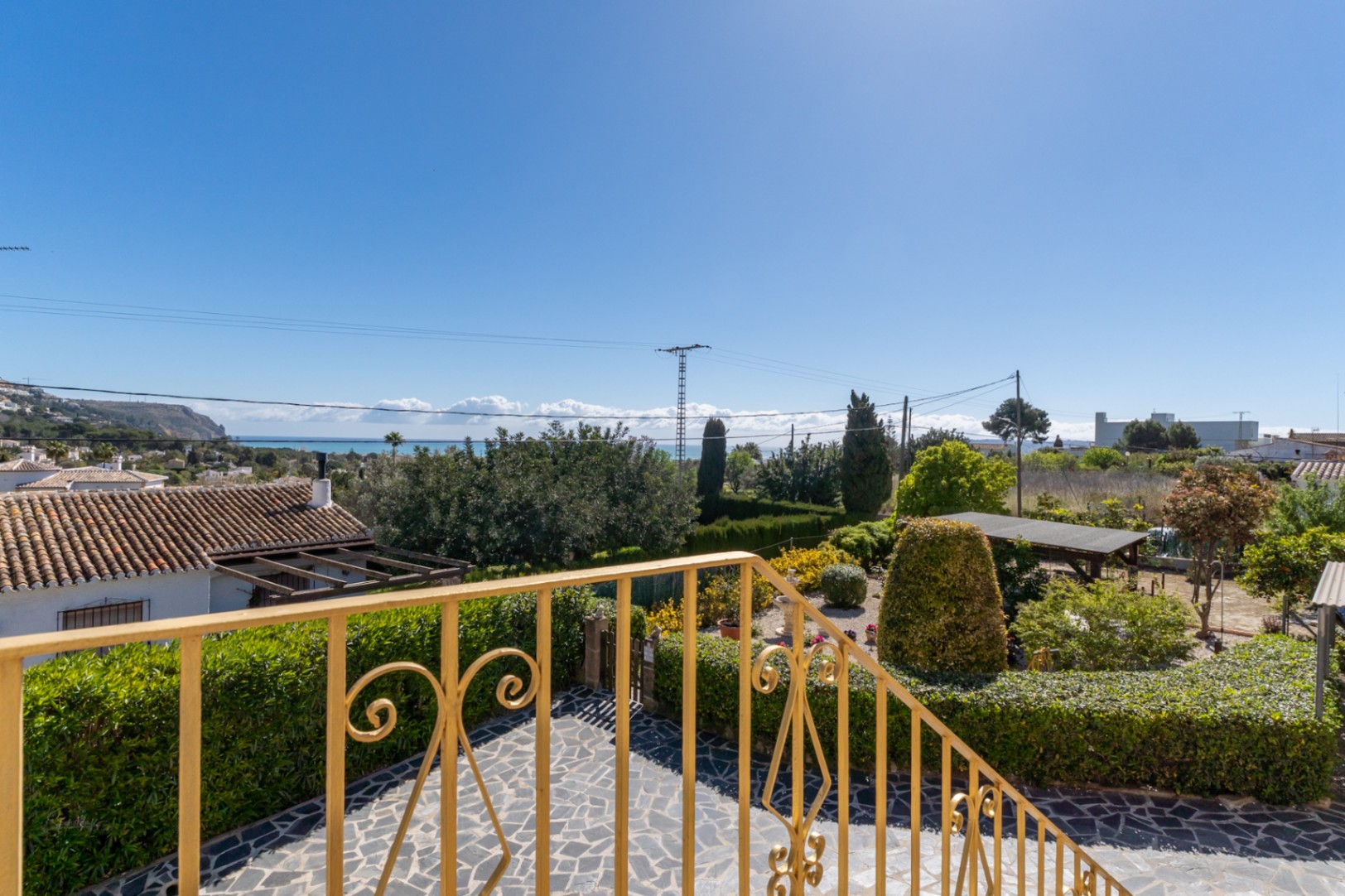 Vue surélevée depuis la terrasse avec garde-corps ornemental, surplombant le jardin méditerranéen et offrant une vue dégagée sur la mer à l'horizon.