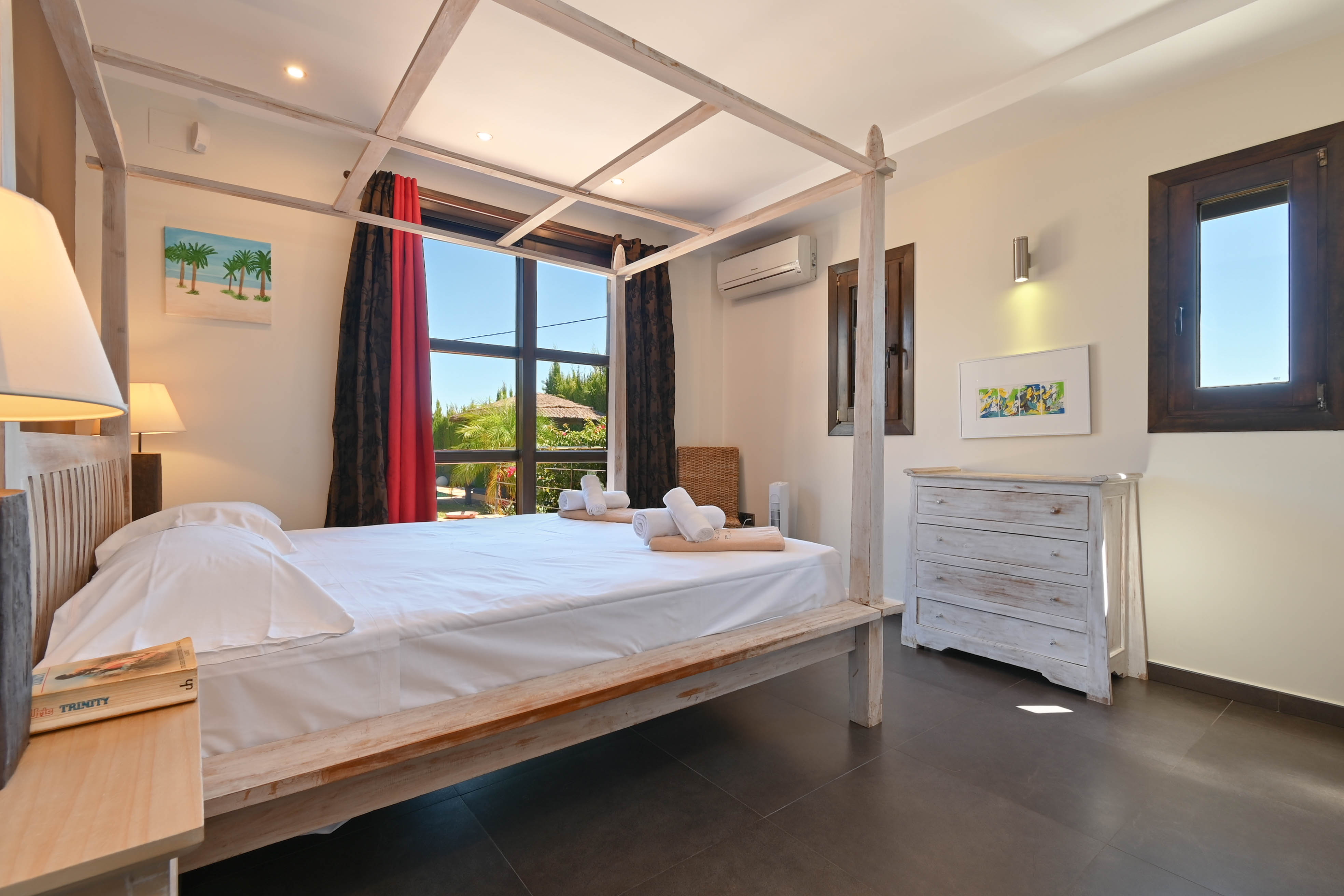 Chambre lumineuse avec lit à baldaquin en bois clair et commode blanche patinée.