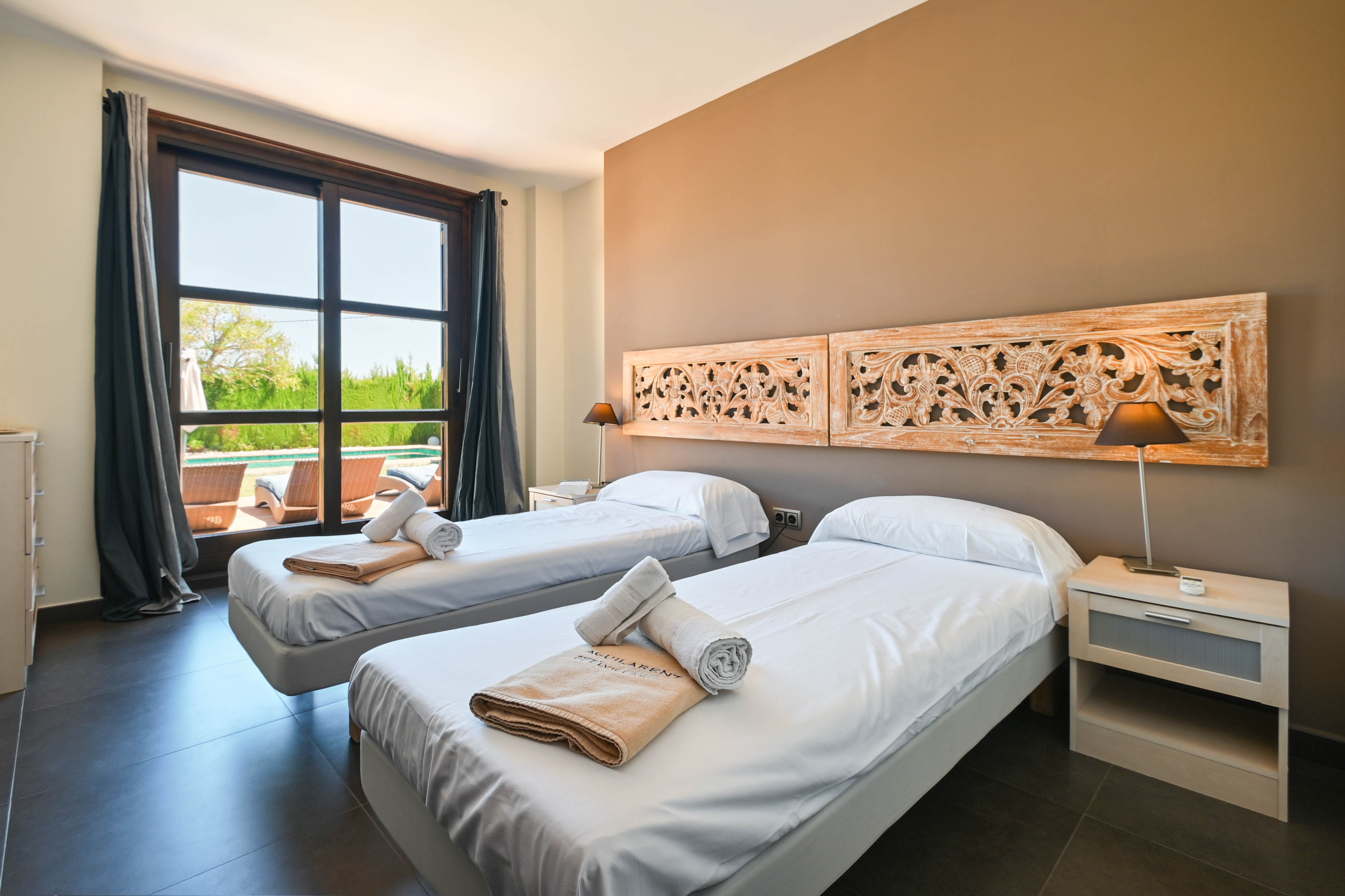 Chambre lumineuse avec lits jumeaux, têtes de lit en bois sculpté et vue sur la piscine.