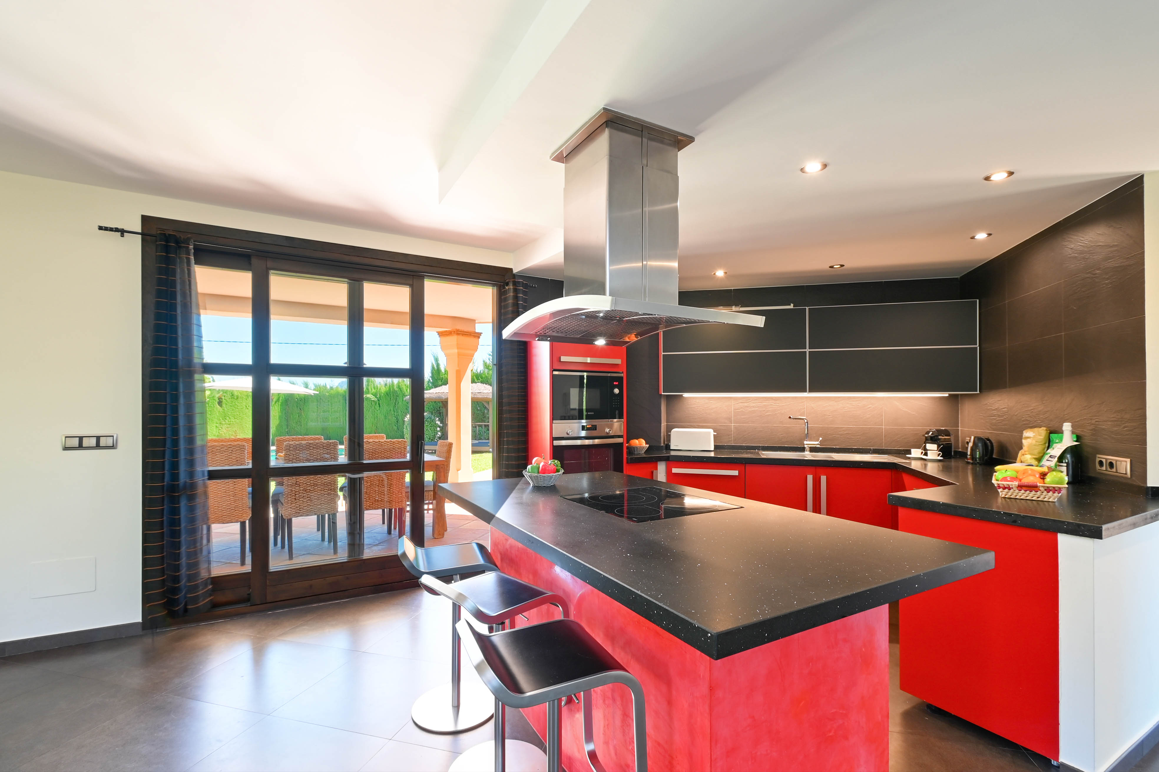 Cuisine moderne avec îlot central, comptoir en granit noir et tabourets en métal.
