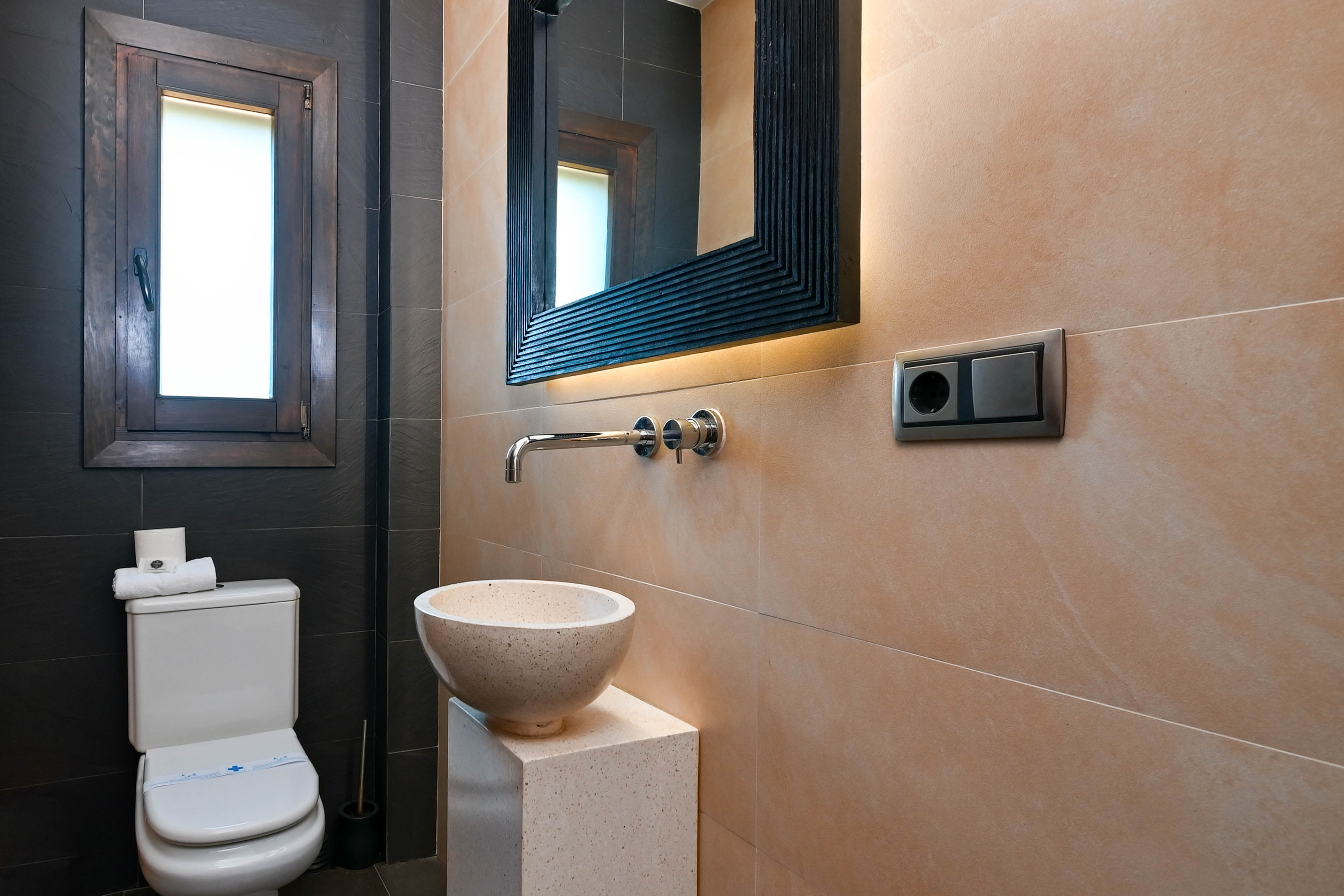 Détail de salle de bain avec lavabo en pierre sur piédestal et miroir à éclairage intégré.