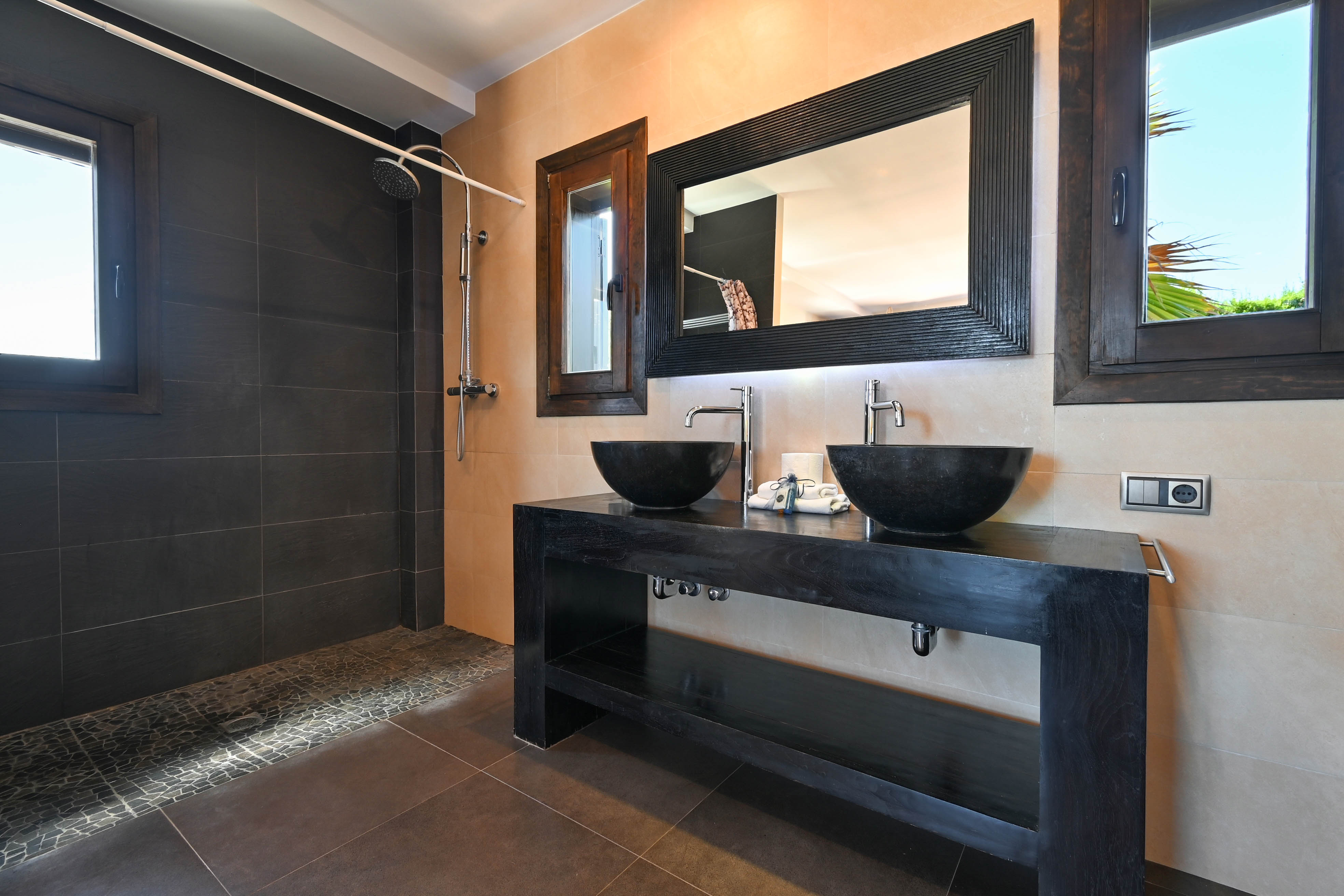 Détail d'une salle de bain moderne avec double vasque en pierre et douche carrelée sombre.