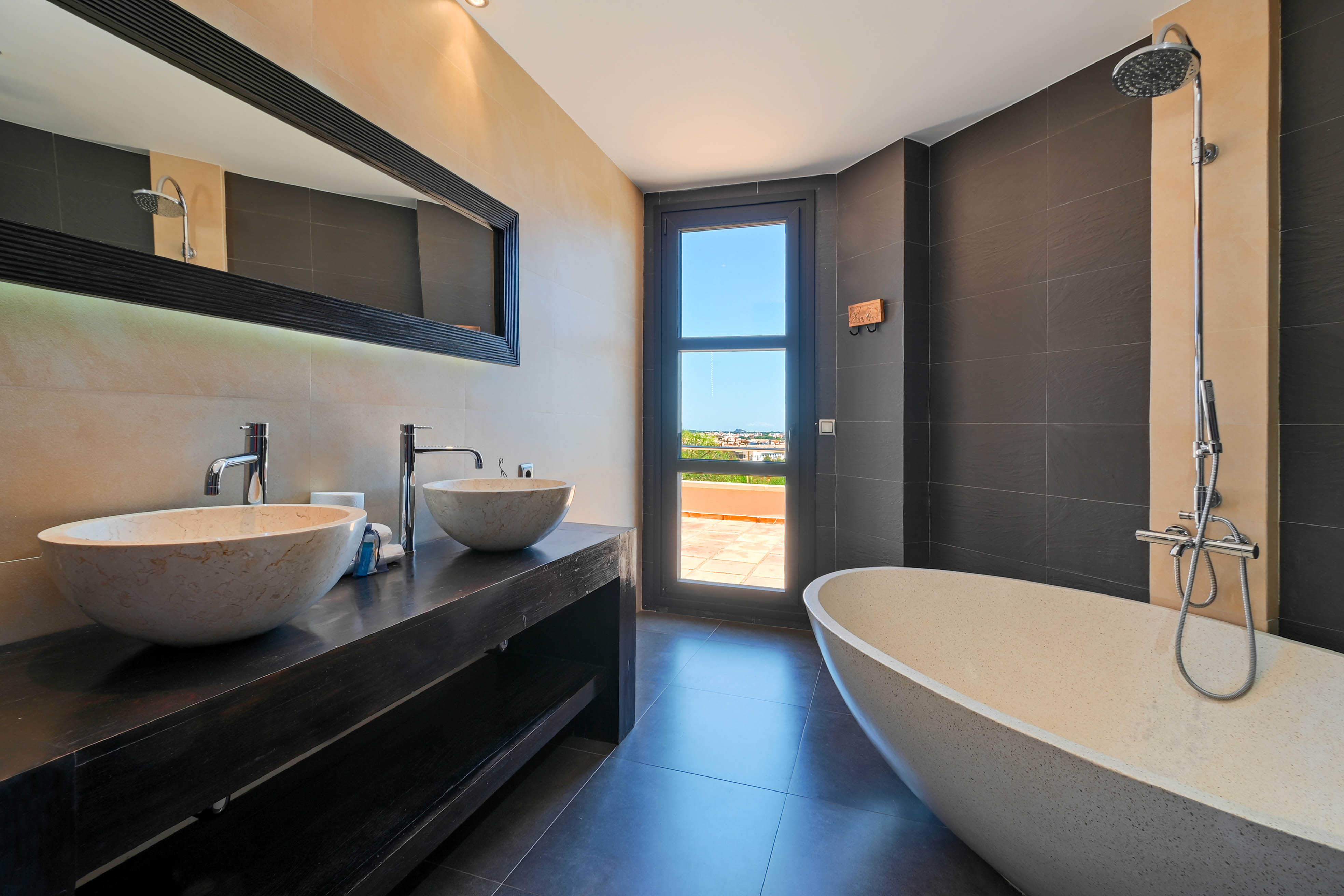Élégante salle de bain avec double vasque en pierre et baignoire îlot, avec accès à une terrasse extérieure.