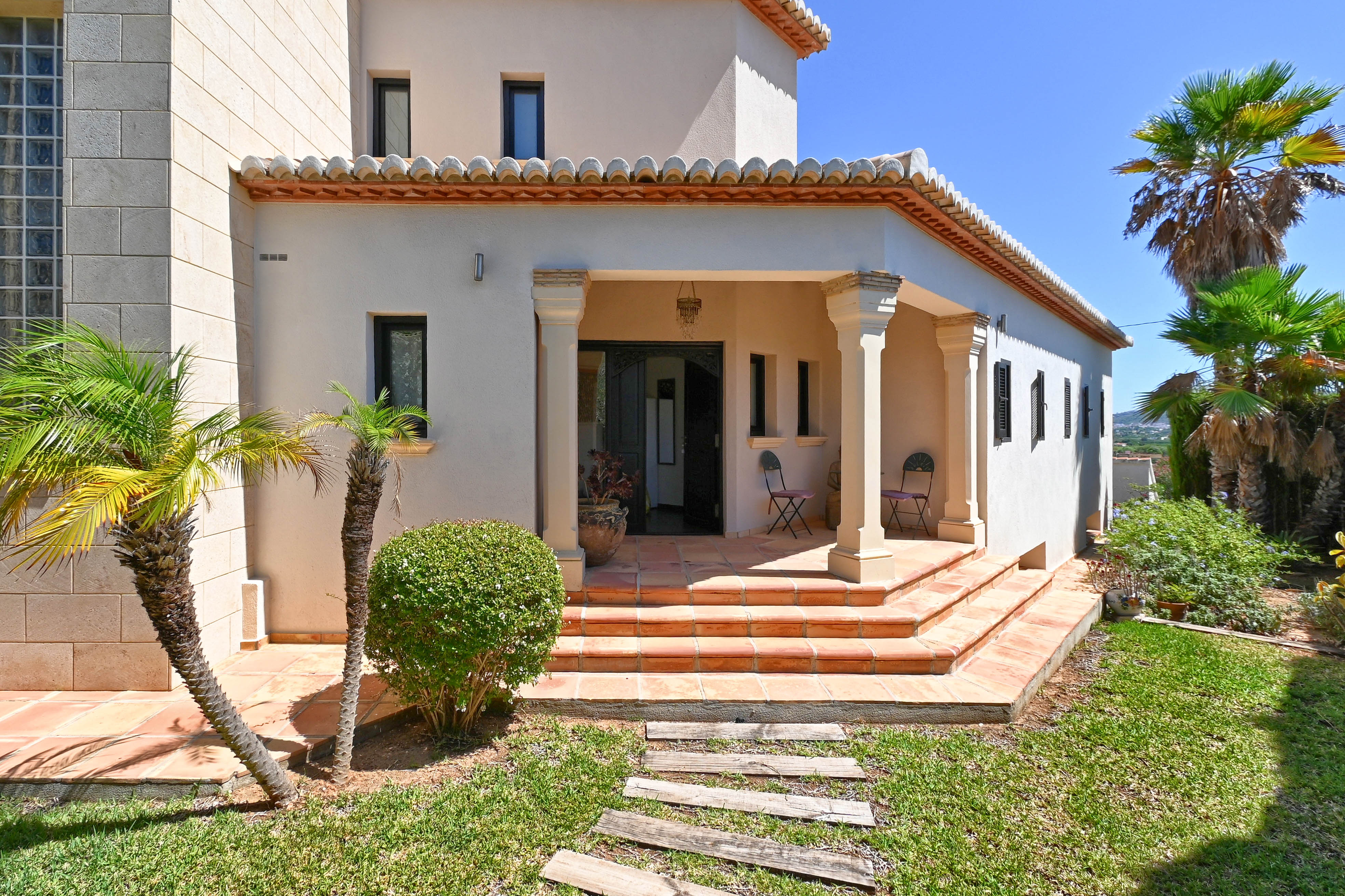 Entrée principale de la villa avec marches en terre cuite et jardin paysager avec palmiers.