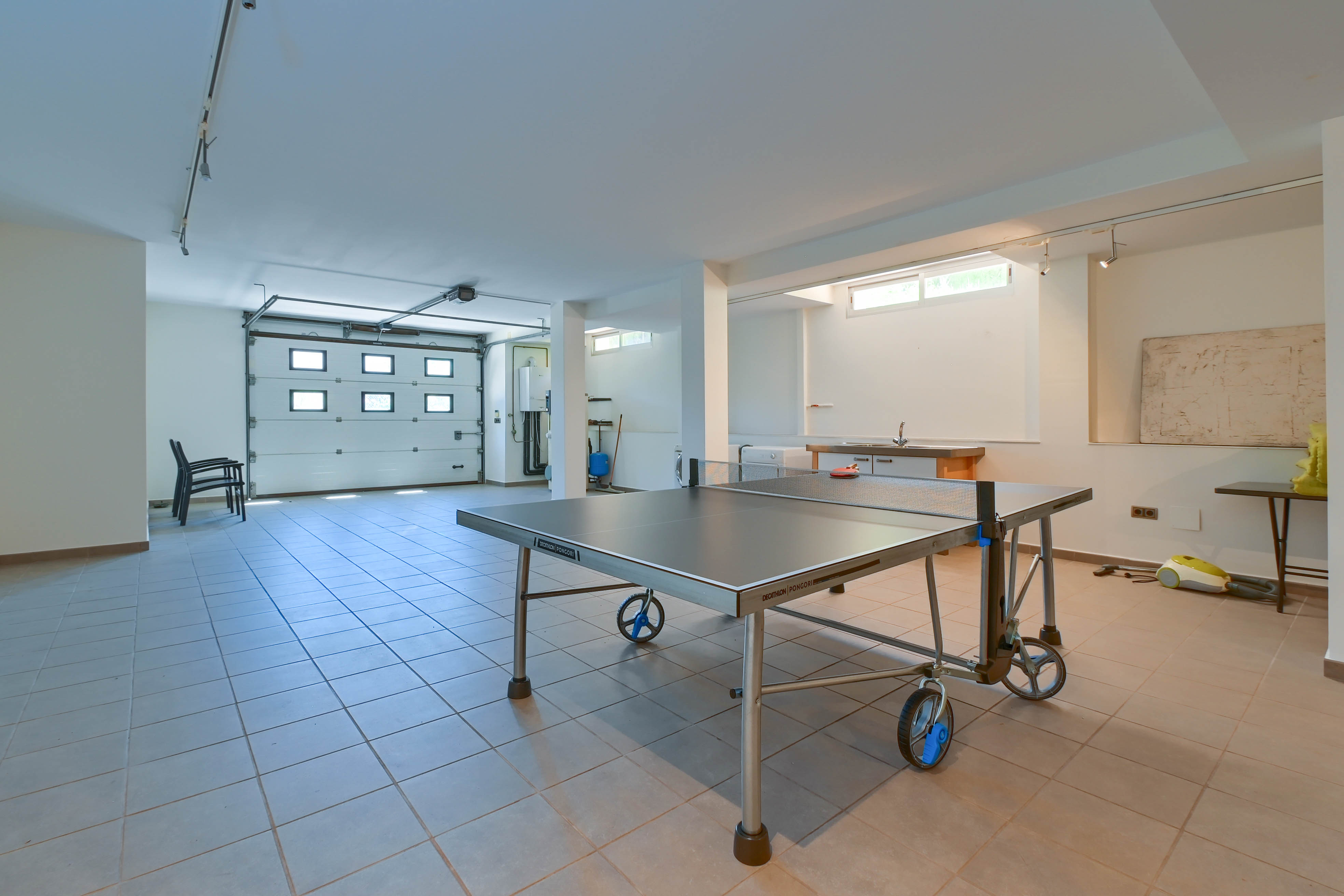 Espace de loisirs avec table de ping-pong Decathlon Pongori, sol carrelé et accès au garage.
