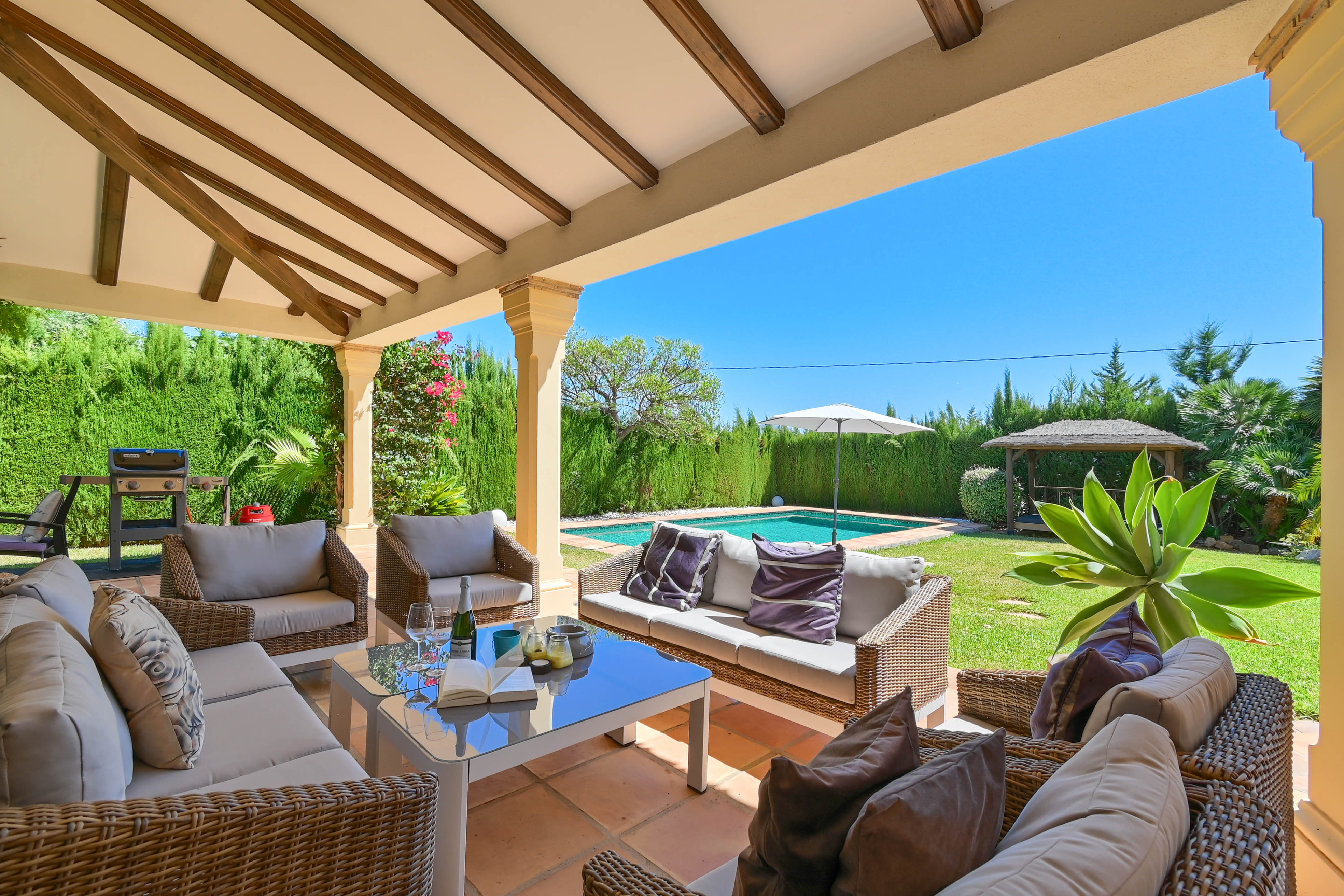 Porche meublé avec des canapés en osier donnant sur la piscine et le jardin.